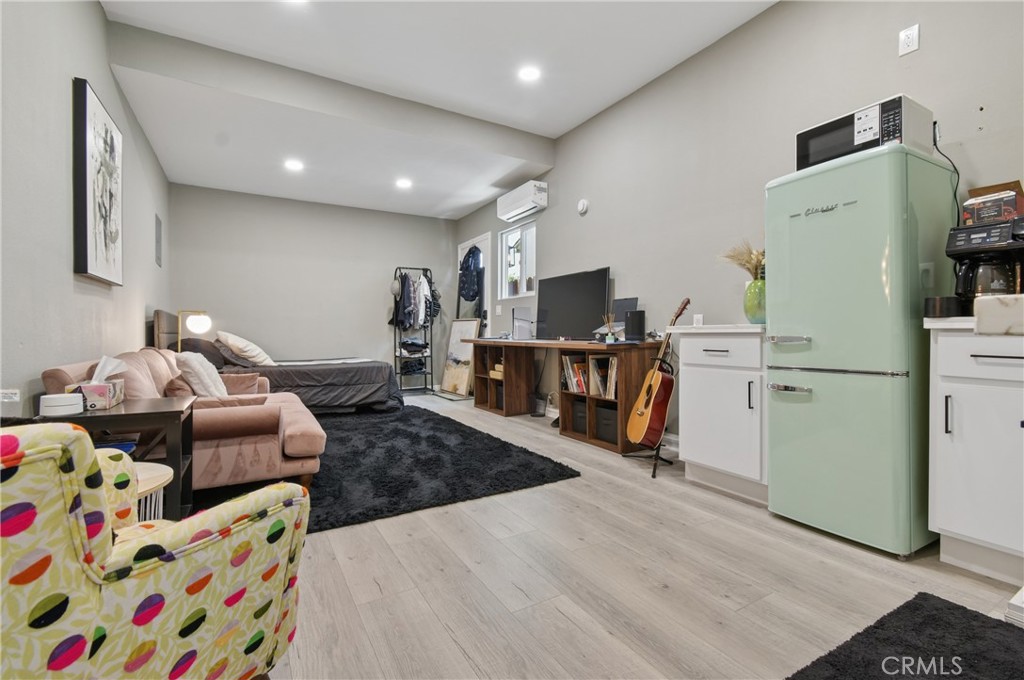 Furnished studio living area with a mint-green refrigerator, desk, guitar, and colorful armchair.
