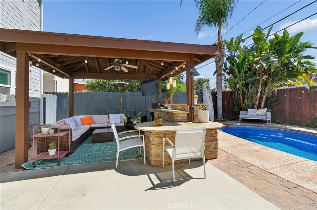 Covered backyard patio with pergola seating, a stone bar, and a swimming pool.