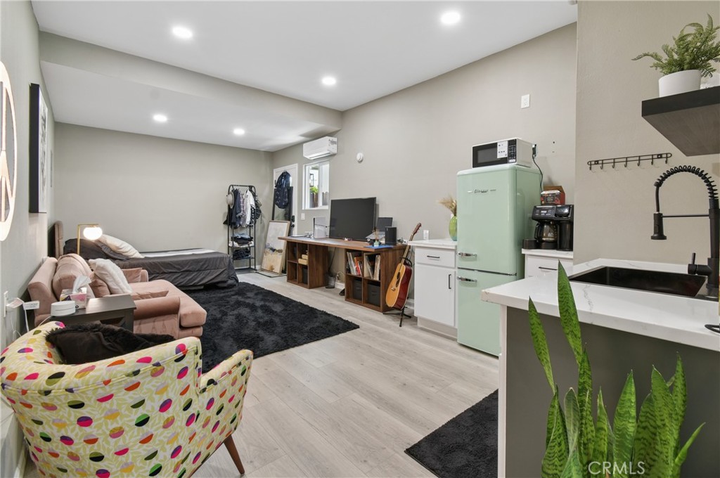 Furnished studio with a compact kitchenette, pale green refrigerator, desk, and sleeping area.