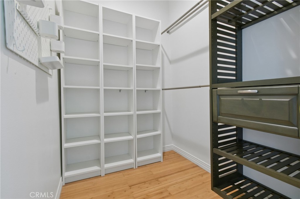 Walk-in closet with white open shelving and dark slatted storage with drawers.
