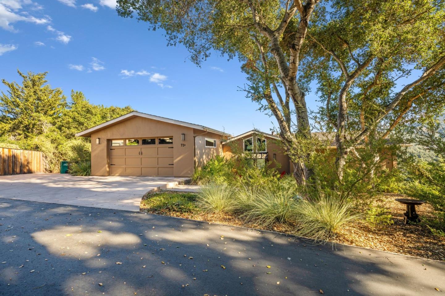 Single-story home with a tan garage and wide driveway beneath mature trees.
