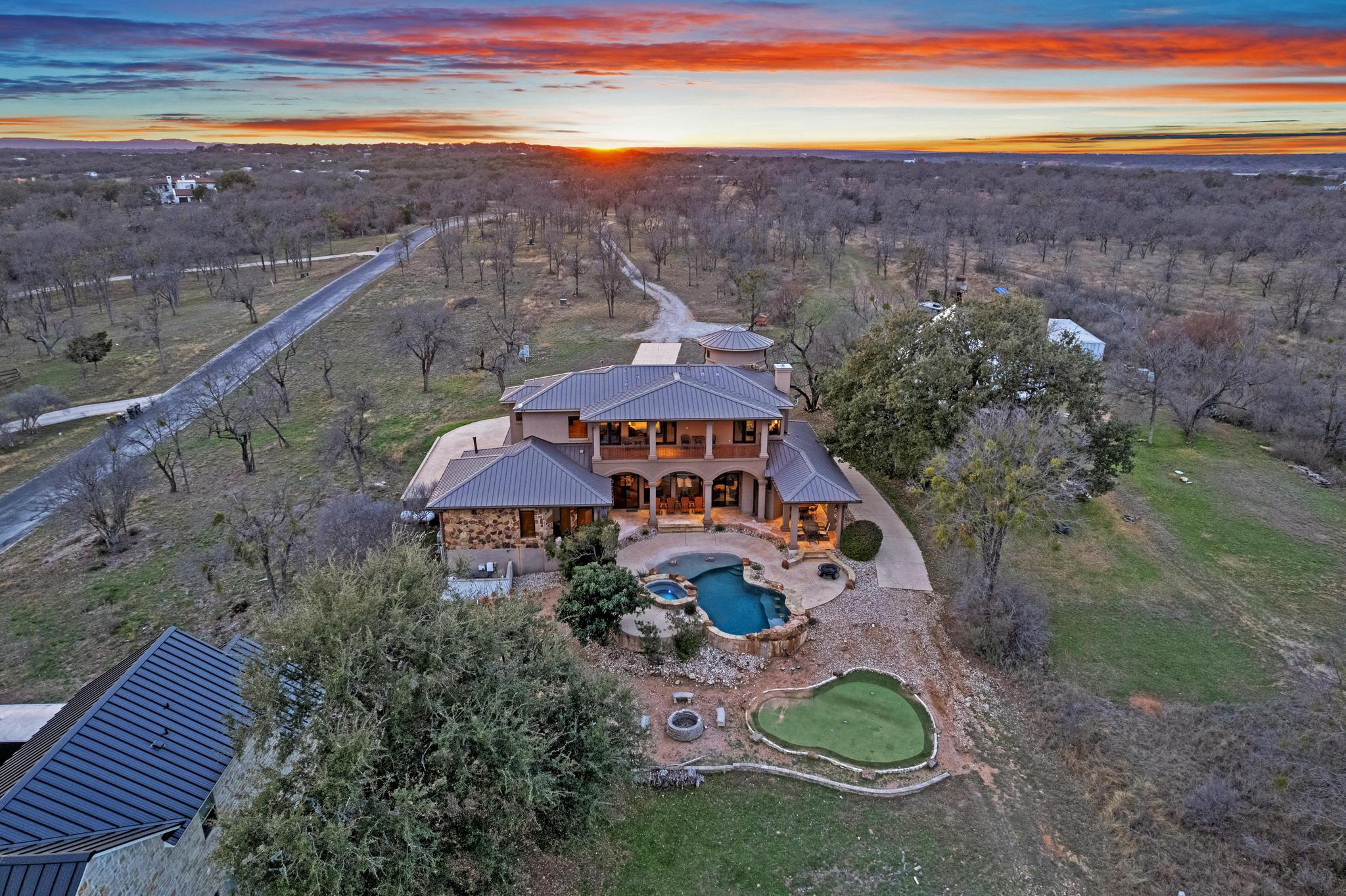 Aerial view of a two-story home with a freeform pool and putting green at sunset.