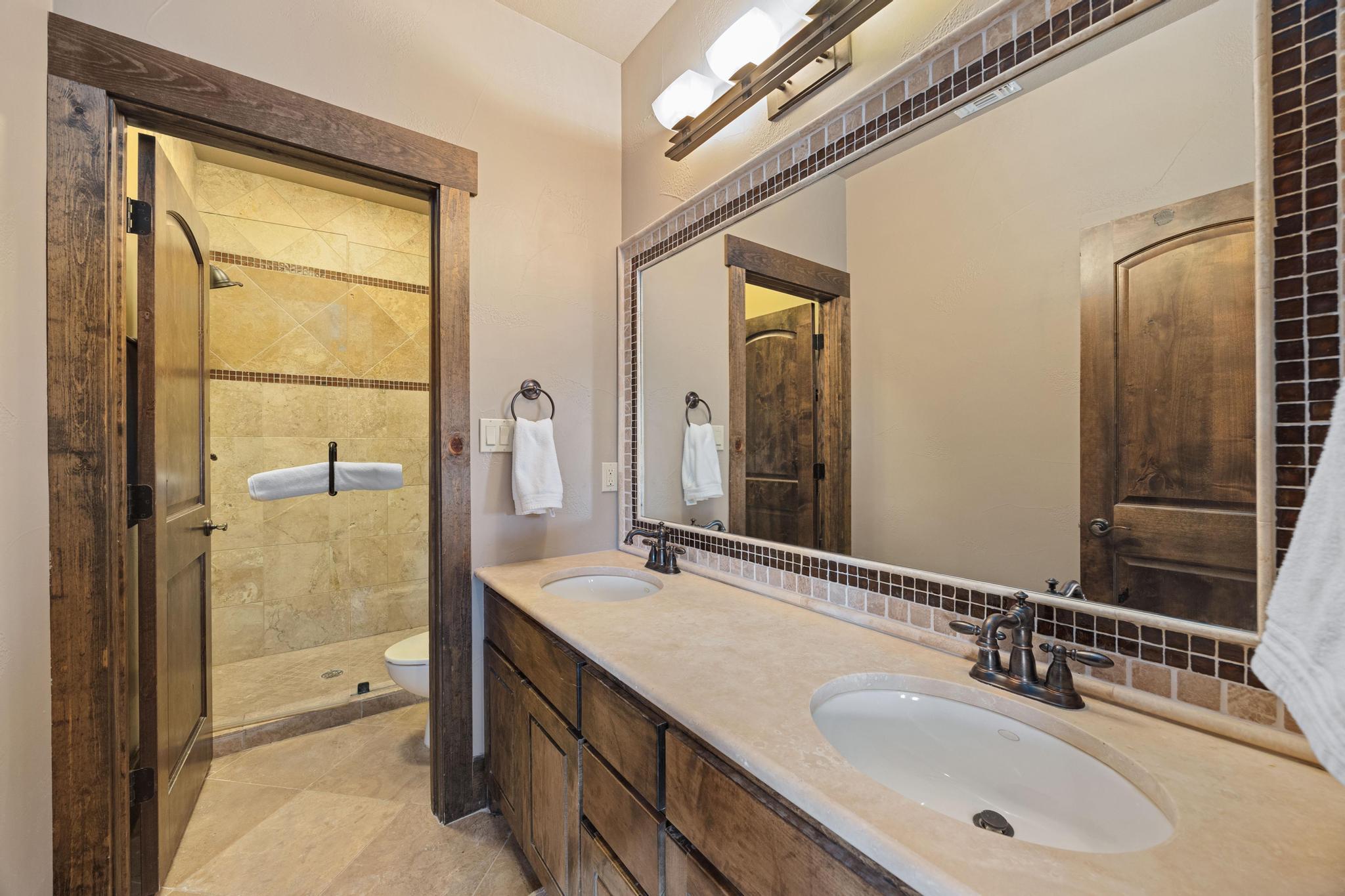 Bathroom with a double-sink vanity, rustic wood cabinetry, and a tiled walk-in shower.