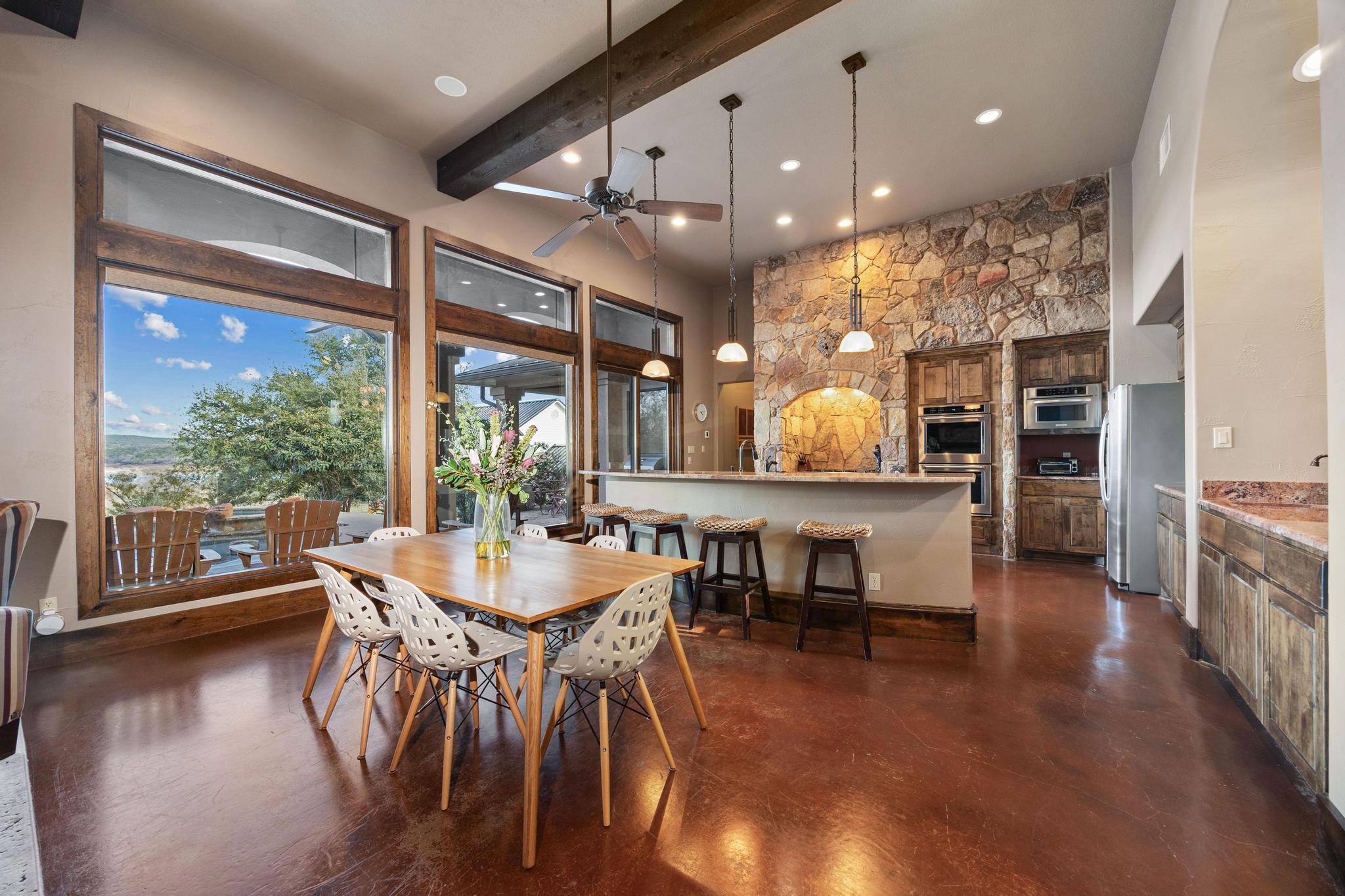 Kitchen and dining area with a stone fireplace wall and large windows overlooking water.