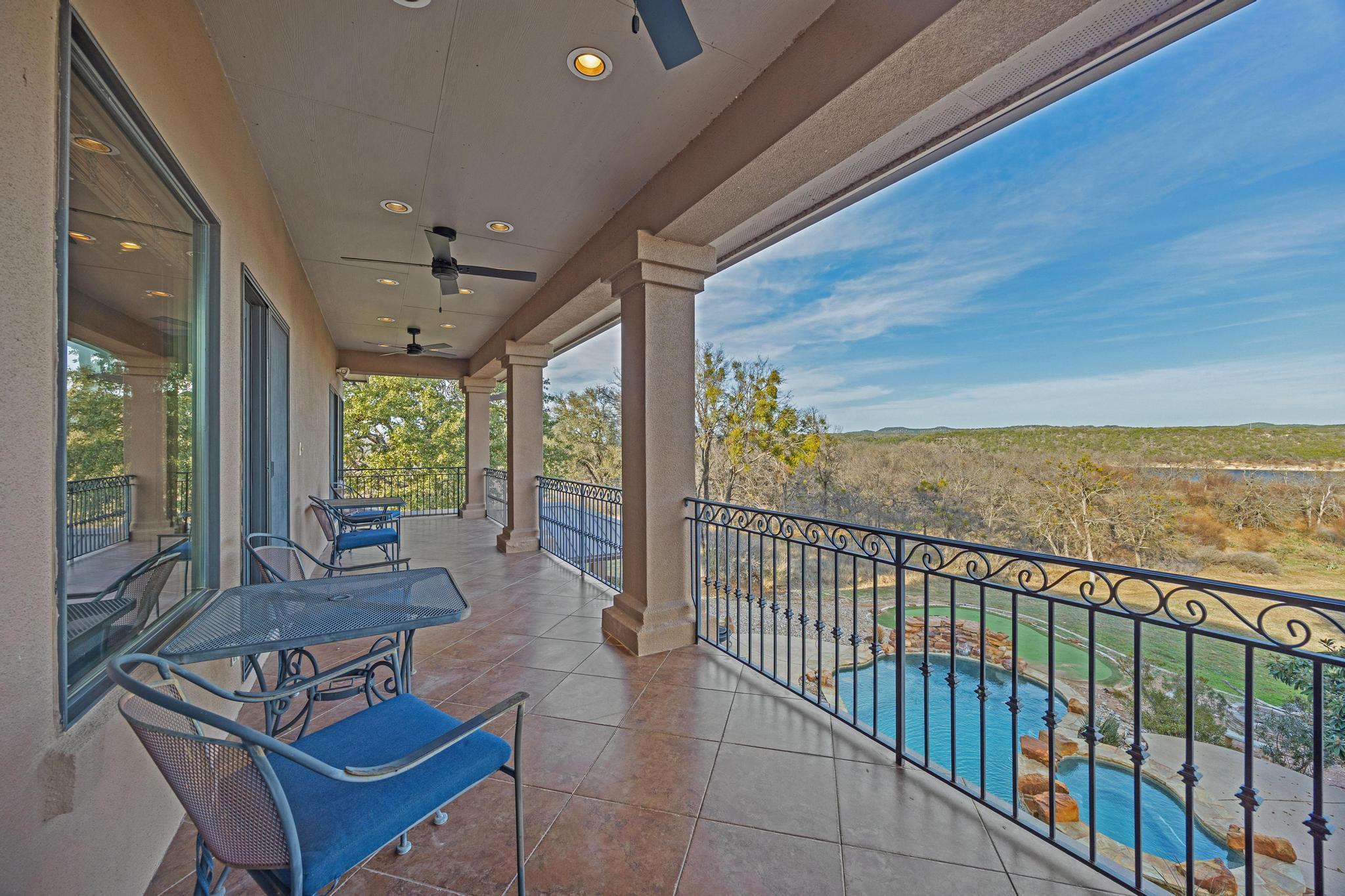 Covered balcony with blue patio furniture overlooking a pool, wooded shoreline, and water.