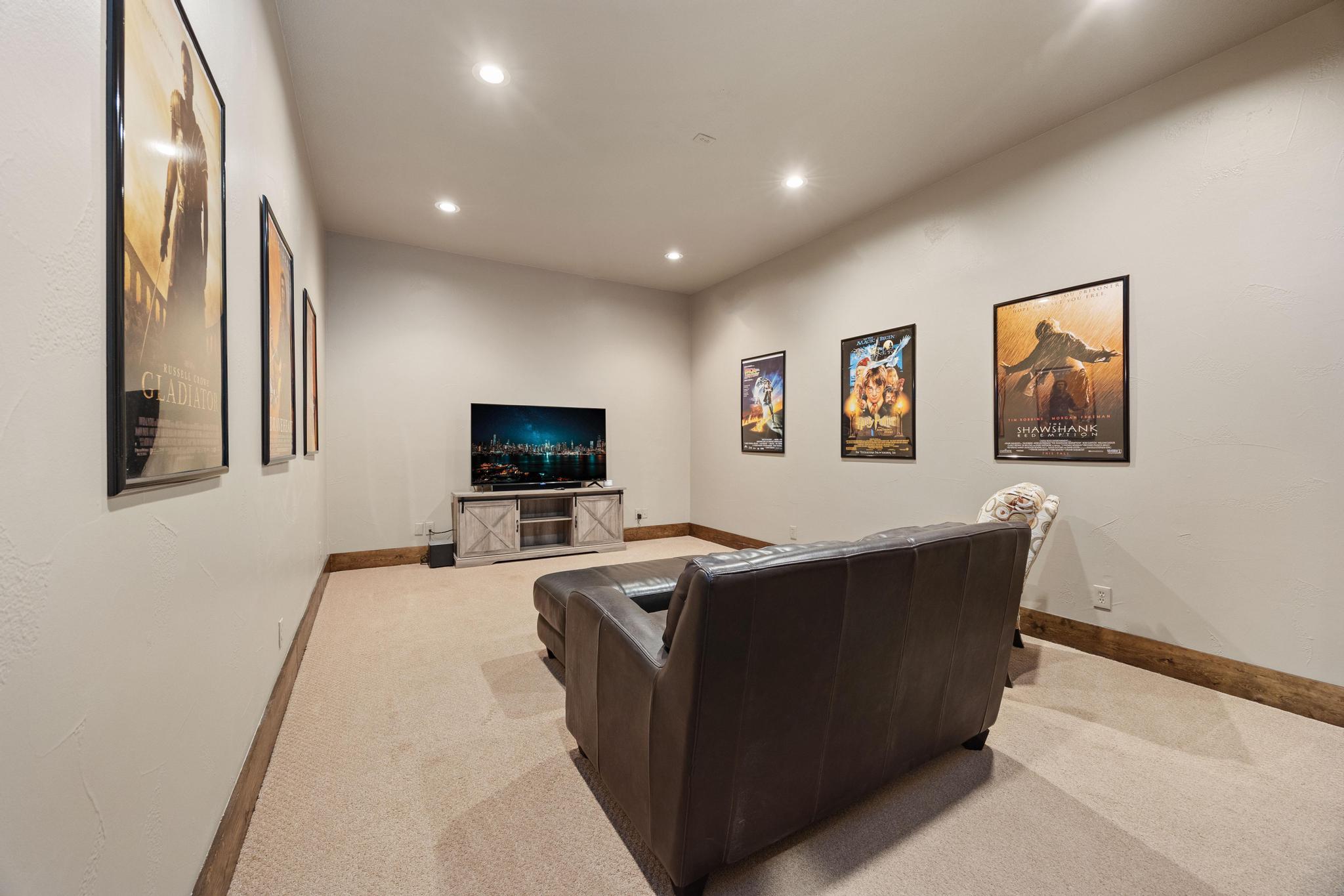 Home theater with a leather sofa facing a television, surrounded by framed movie posters.