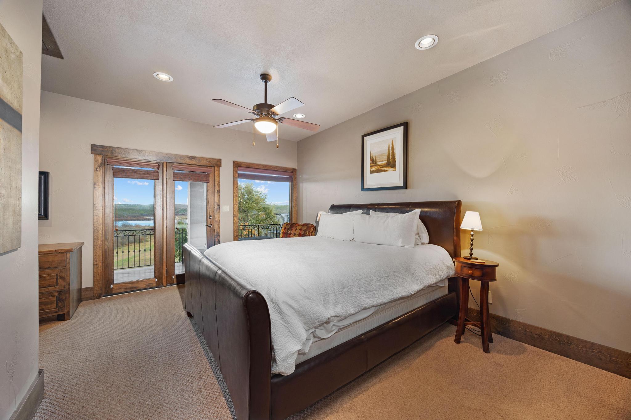Bedroom with a large leather bed and wood-trimmed doors overlooking water and rolling hills.