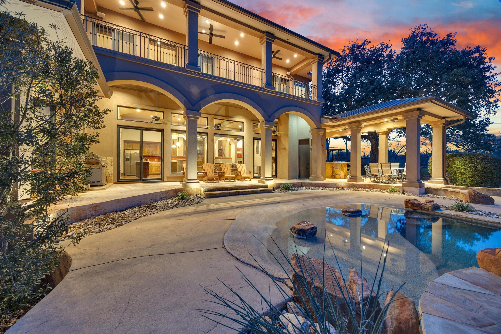 Two-story home with arched balconies and a pool at dusk.