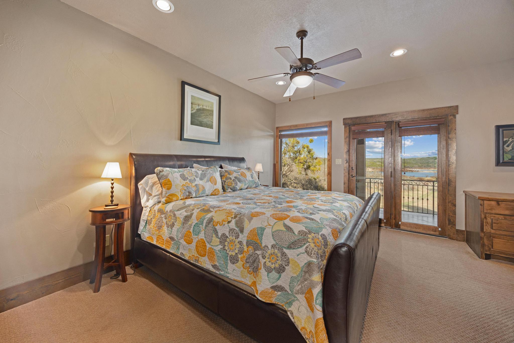 Furnished bedroom with a floral quilted bed and balcony doors overlooking a lake.