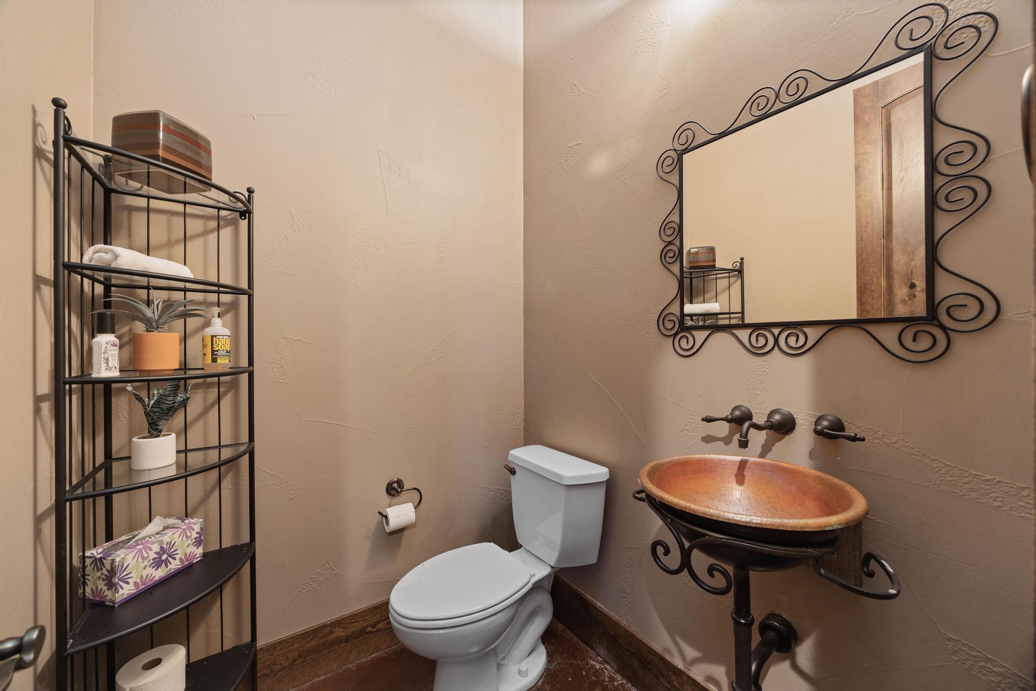 Bathroom with a copper vessel sink, ornate mirror, and black metal shelving.