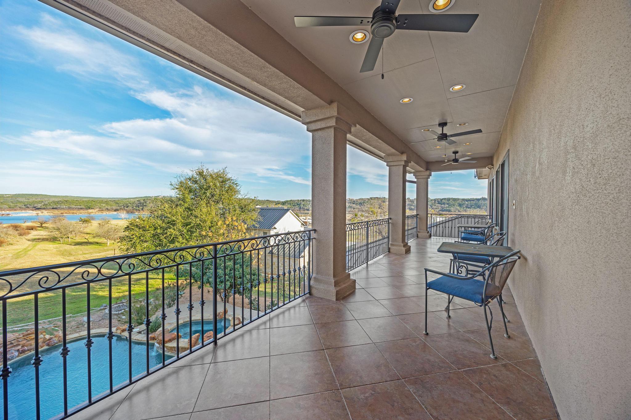 Covered tiled balcony with wrought-iron railing and seating overlooking a pool and lake.
