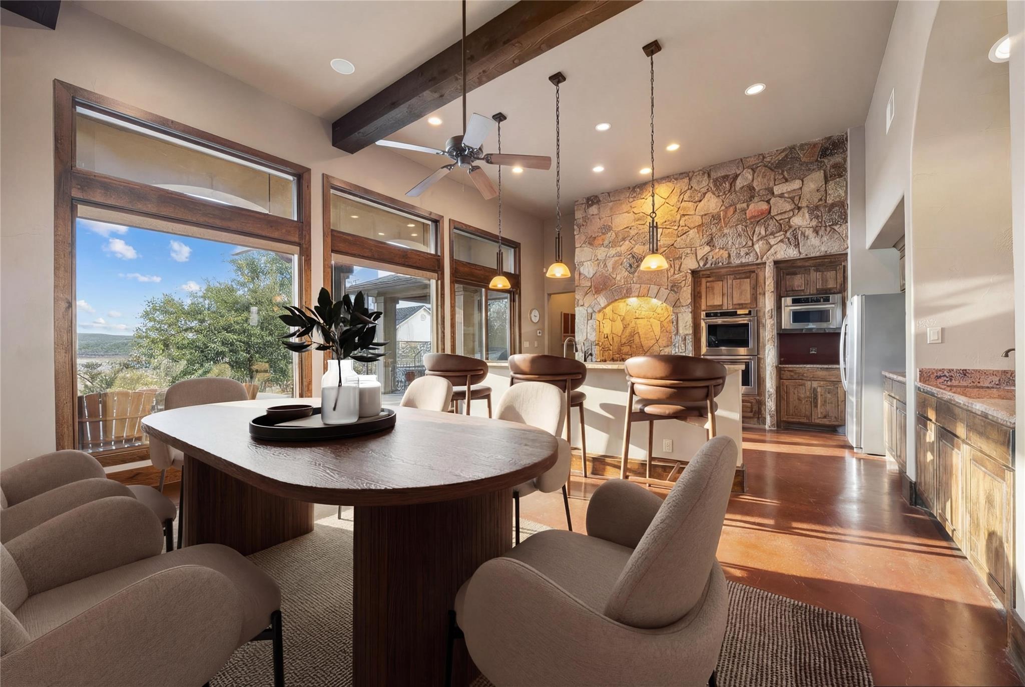 Open-plan kitchen and dining area with a stone fireplace wall and large windows overlooking water.