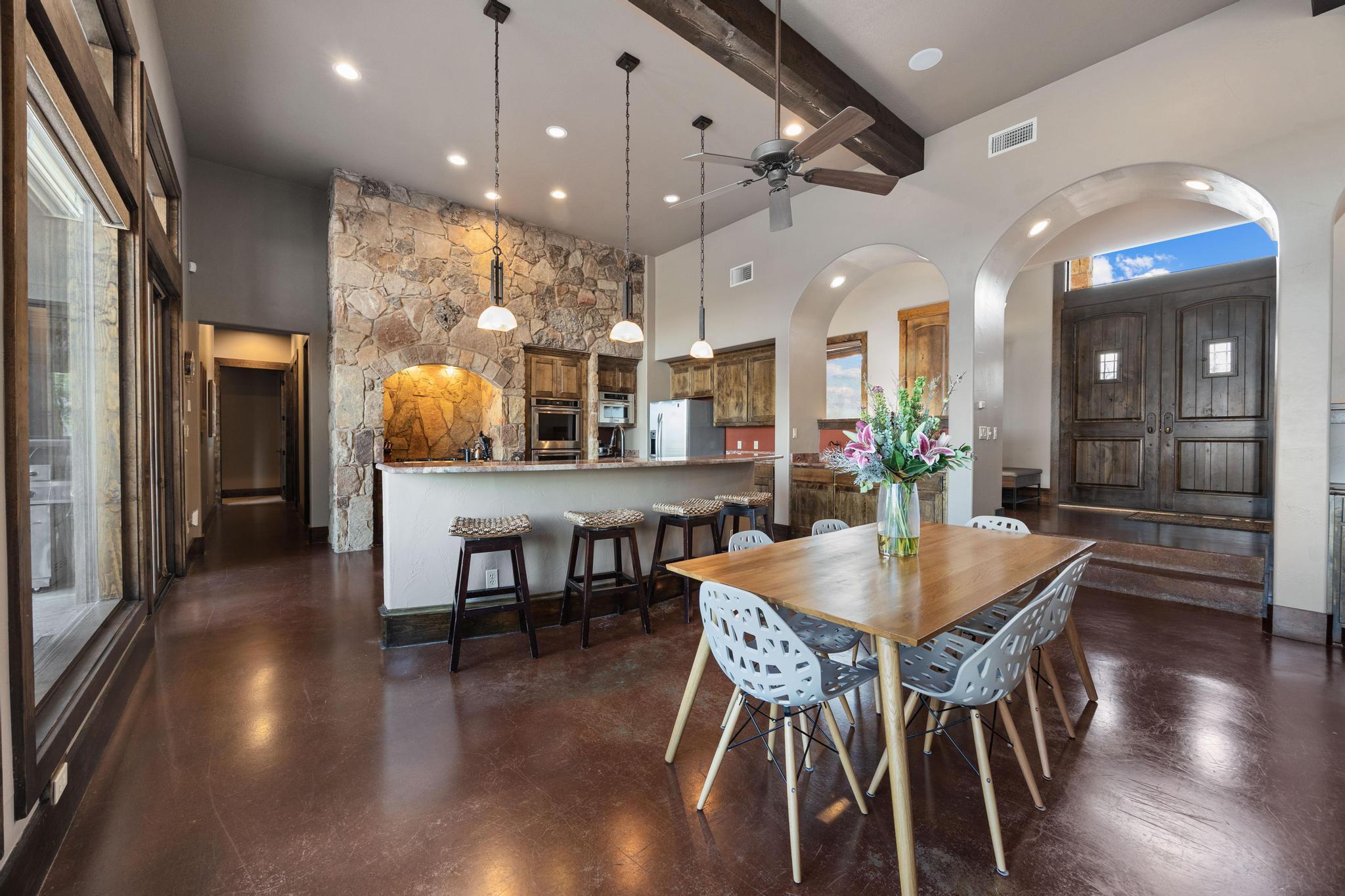 Open kitchen and dining area with a stone feature wall, exposed beams, and arched entry.