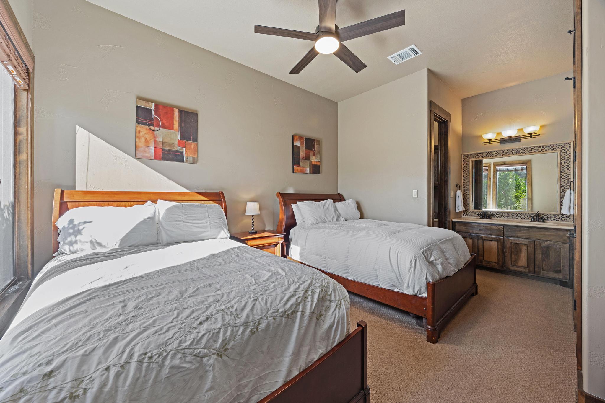 Bedroom with two wooden beds, white bedding, and a dark wood vanity with mosaic-framed mirror.