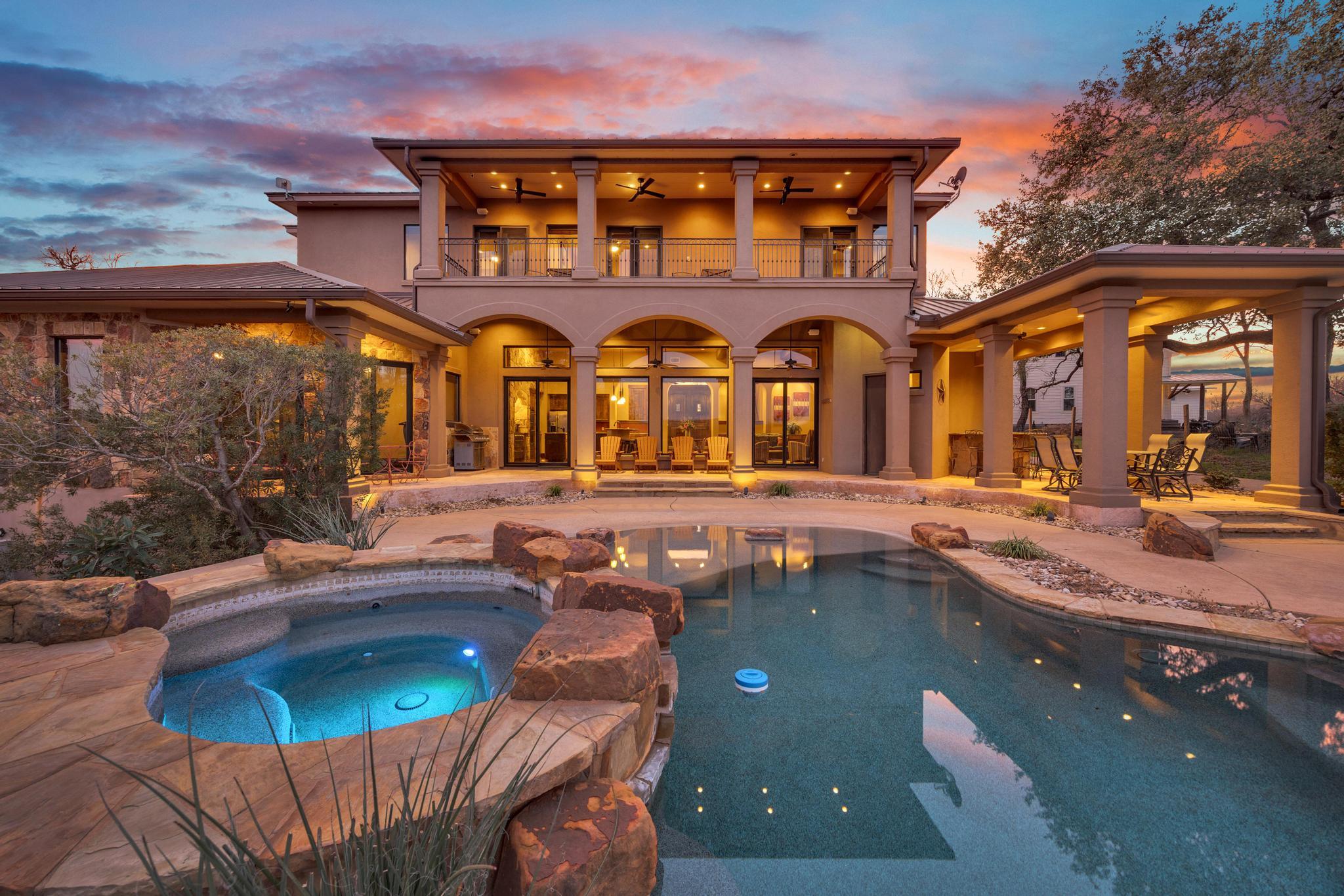 Two-story home with an arched covered patio and illuminated pool at dusk.