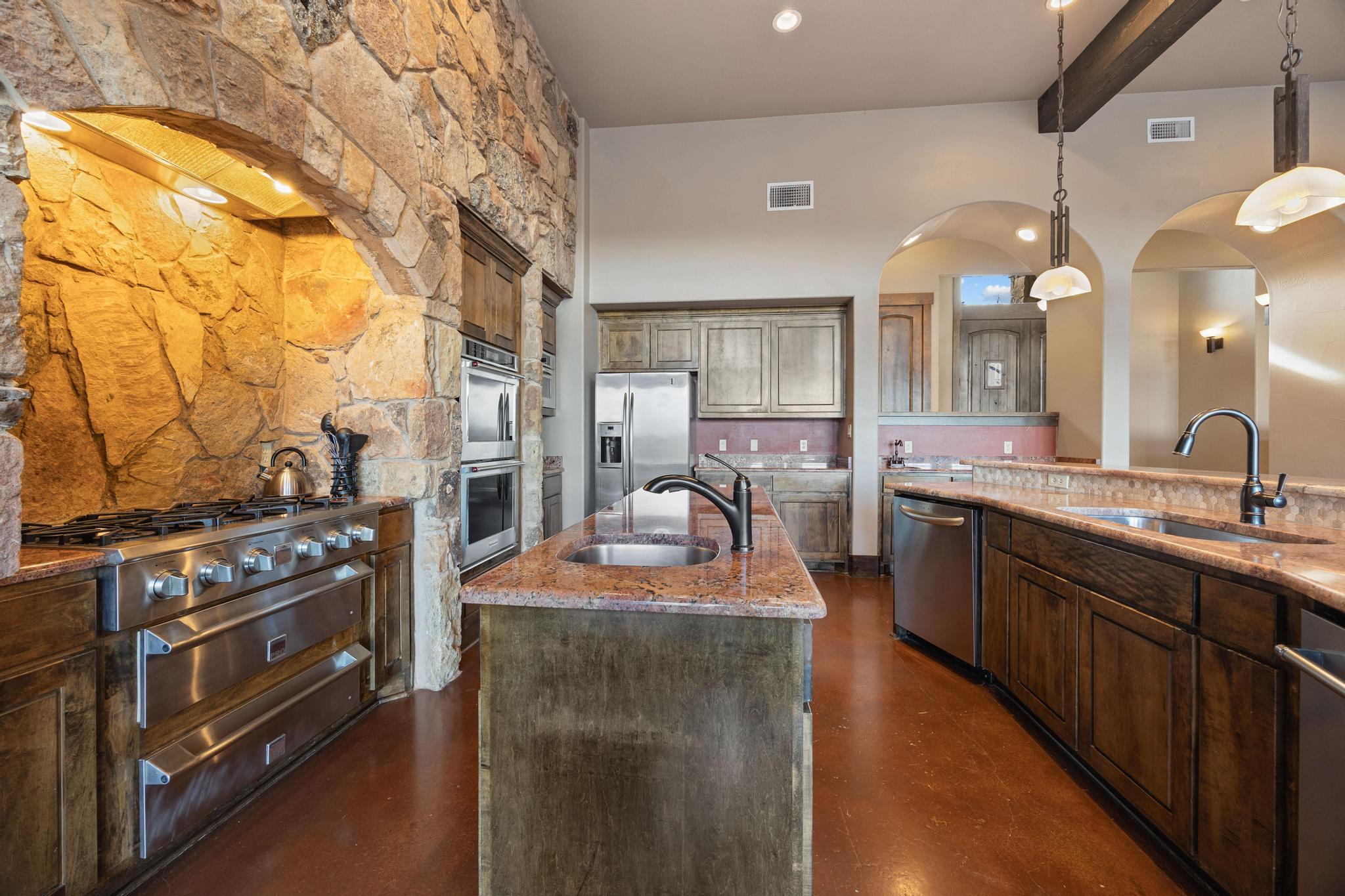 Kitchen with a stone range alcove, stainless steel appliances, and a granite island with sink