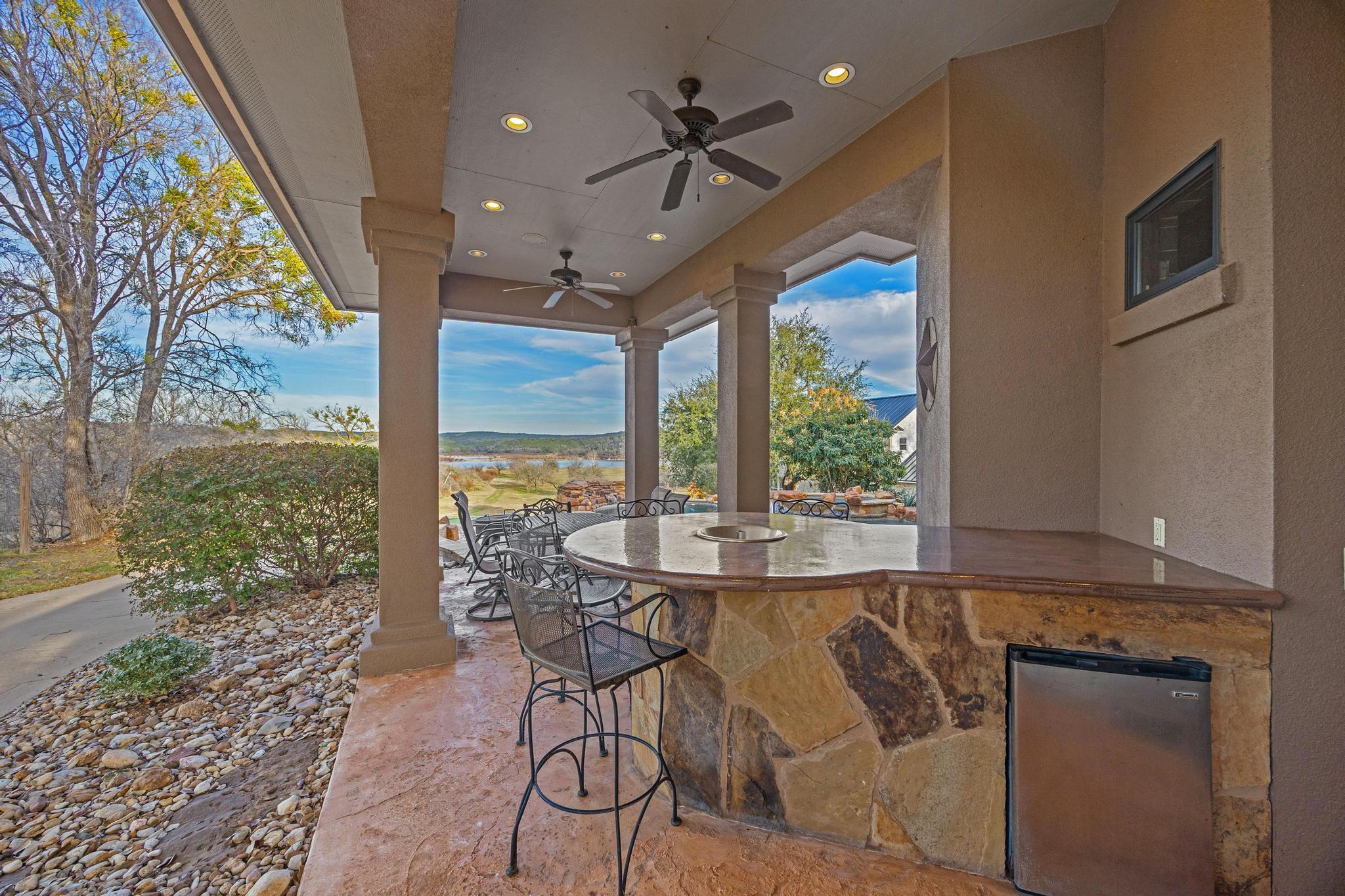 Covered patio with a stone bar and grill, dining chairs, and a lake view.