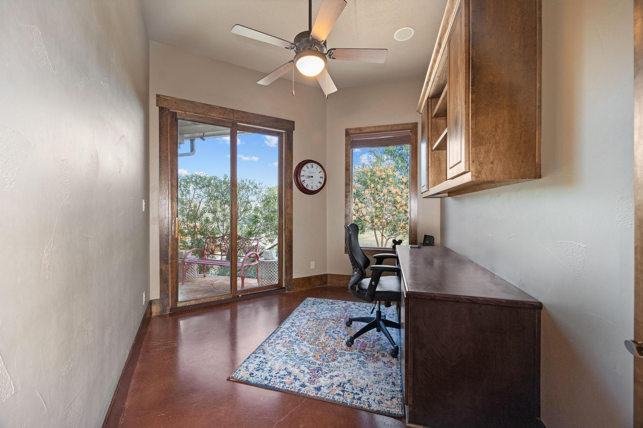 Home office with a long wood desk and built-in cabinets beside sliding glass doors to a patio.