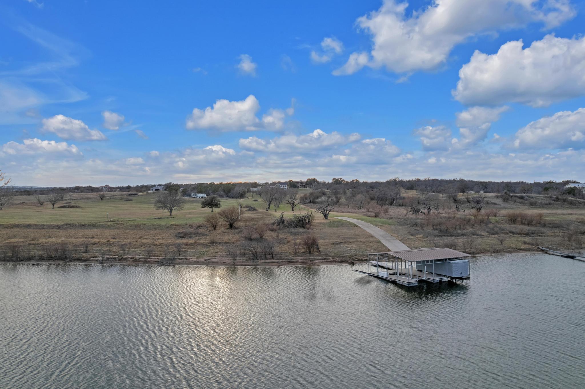 Aerial view of waterfront land with a covered boat dock, curving path, and scattered leafless trees.