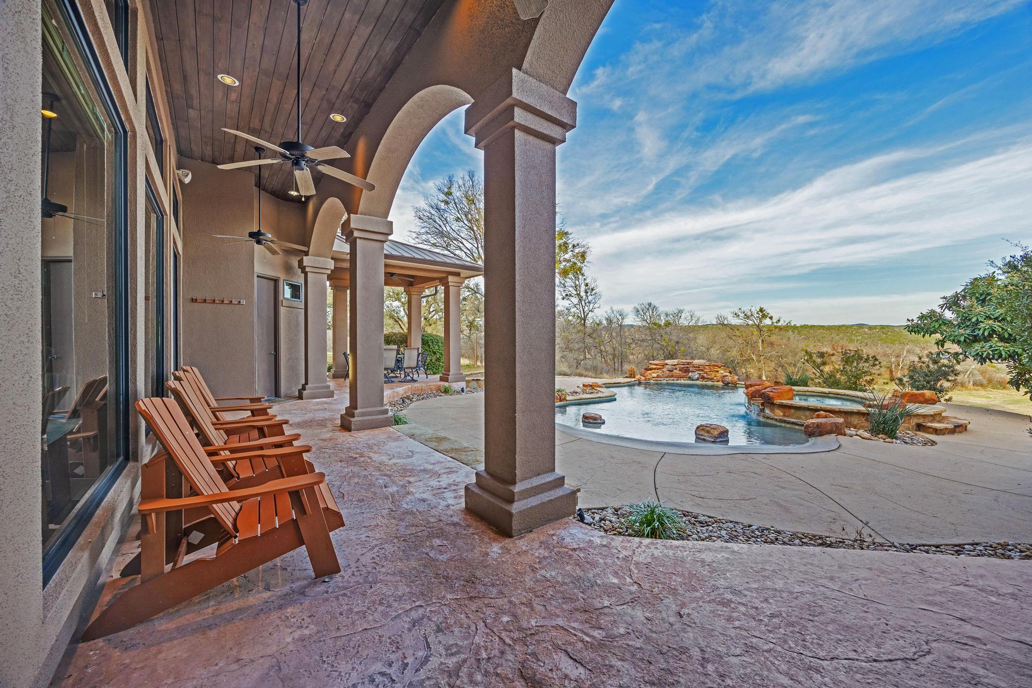 Covered stone patio with arched columns, Adirondack chairs, a freeform pool, and raised rock spa.