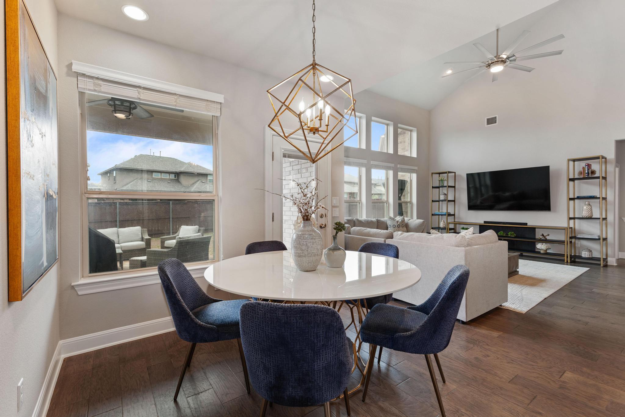 Open-plan dining and living room with a round table, navy chairs, and a geometric brass pendant.