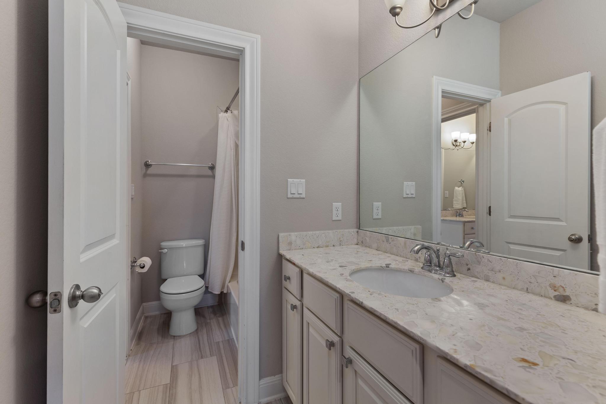 Bathroom with a long stone vanity and large mirror beside a separate toilet area.
