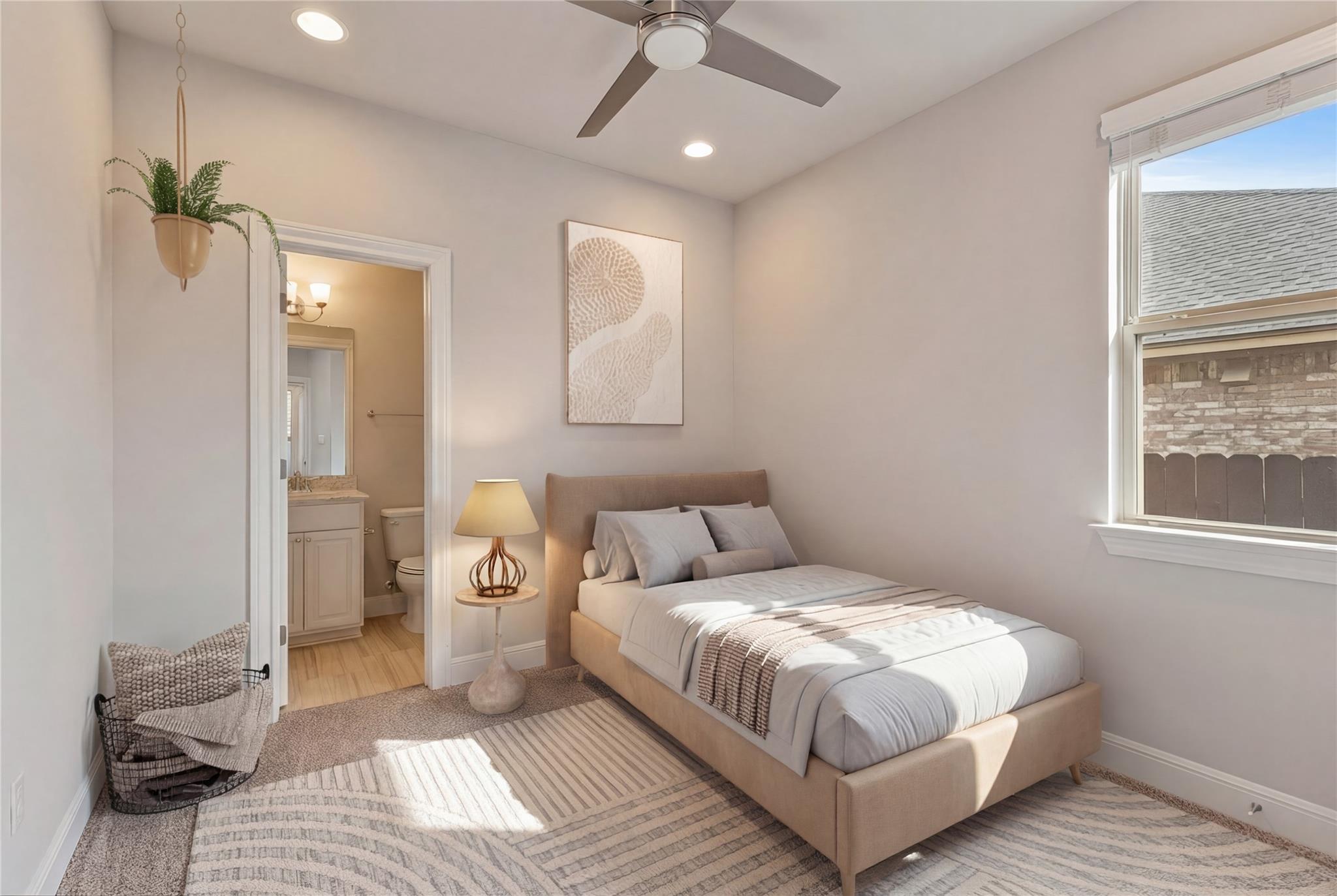 Staged bedroom with an upholstered bed, ceiling fan, and open doorway to an en-suite bathroom.