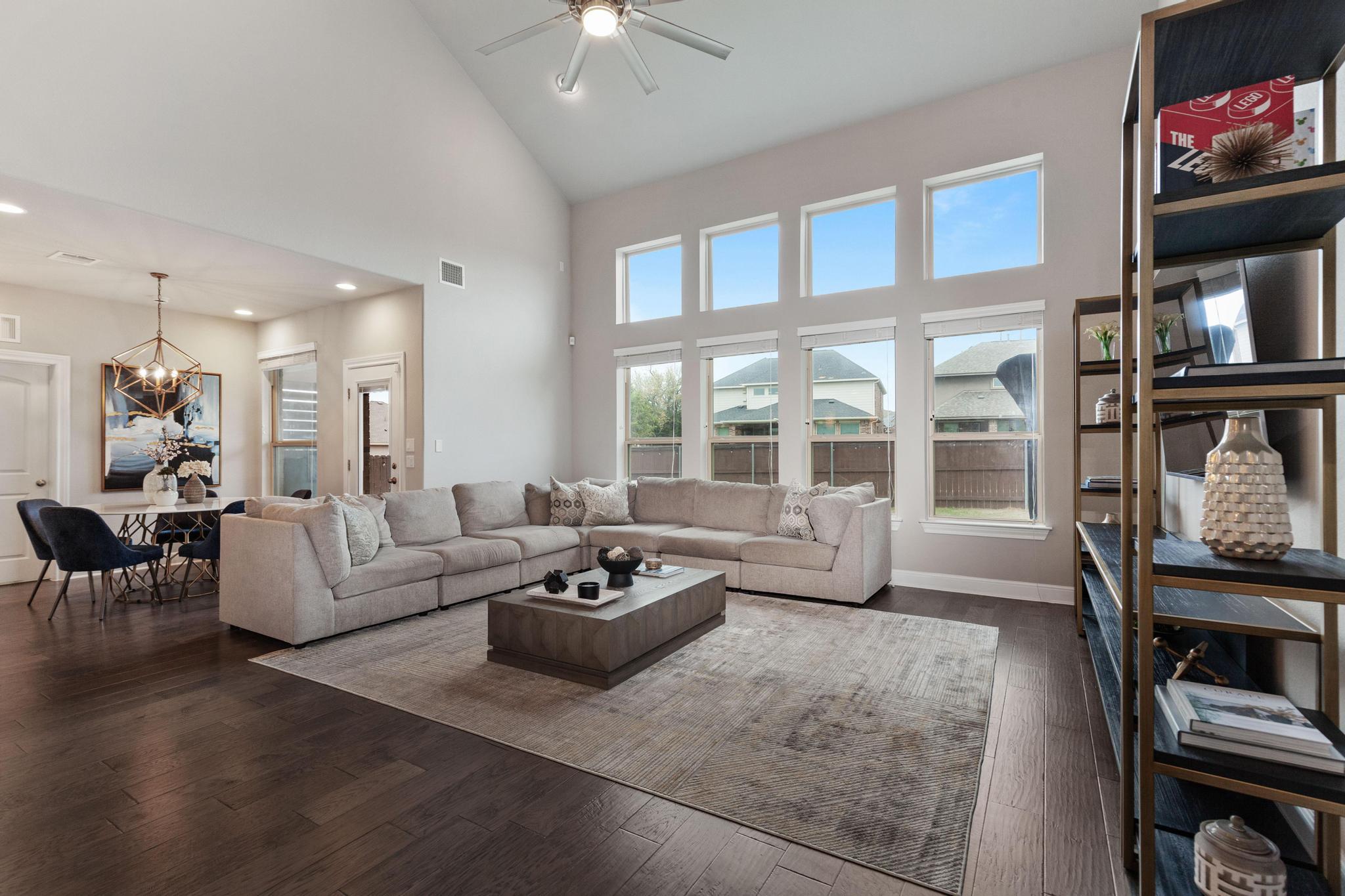 Vaulted living room with a gray sectional sofa, tall windows, and adjoining dining area.