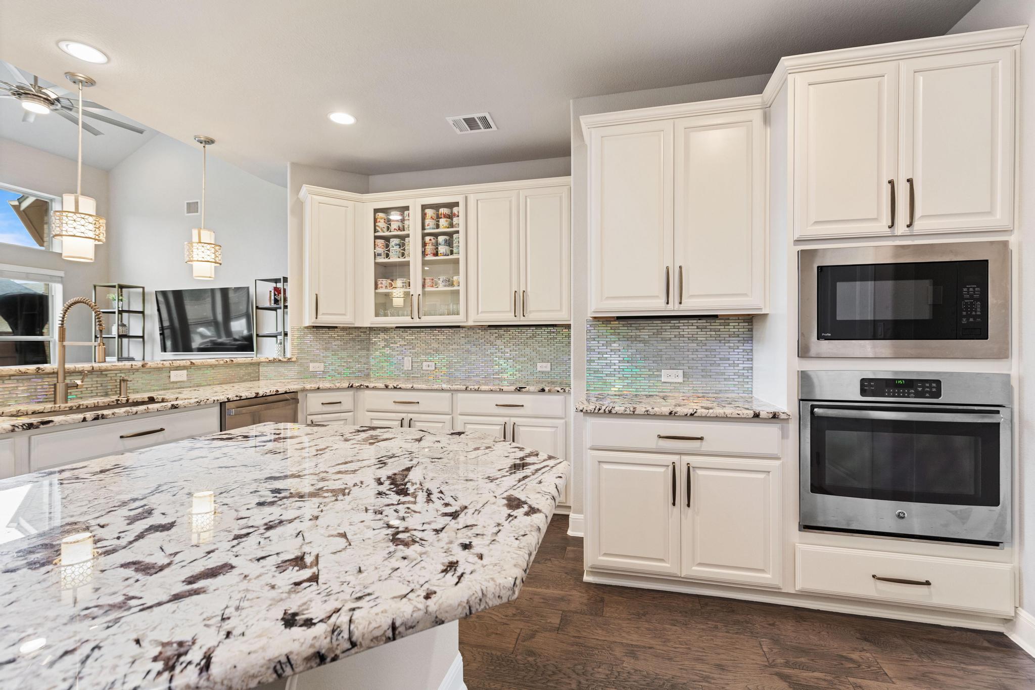 Kitchen with a large patterned granite island, white cabinets, iridescent backsplash, and built-in appliances.