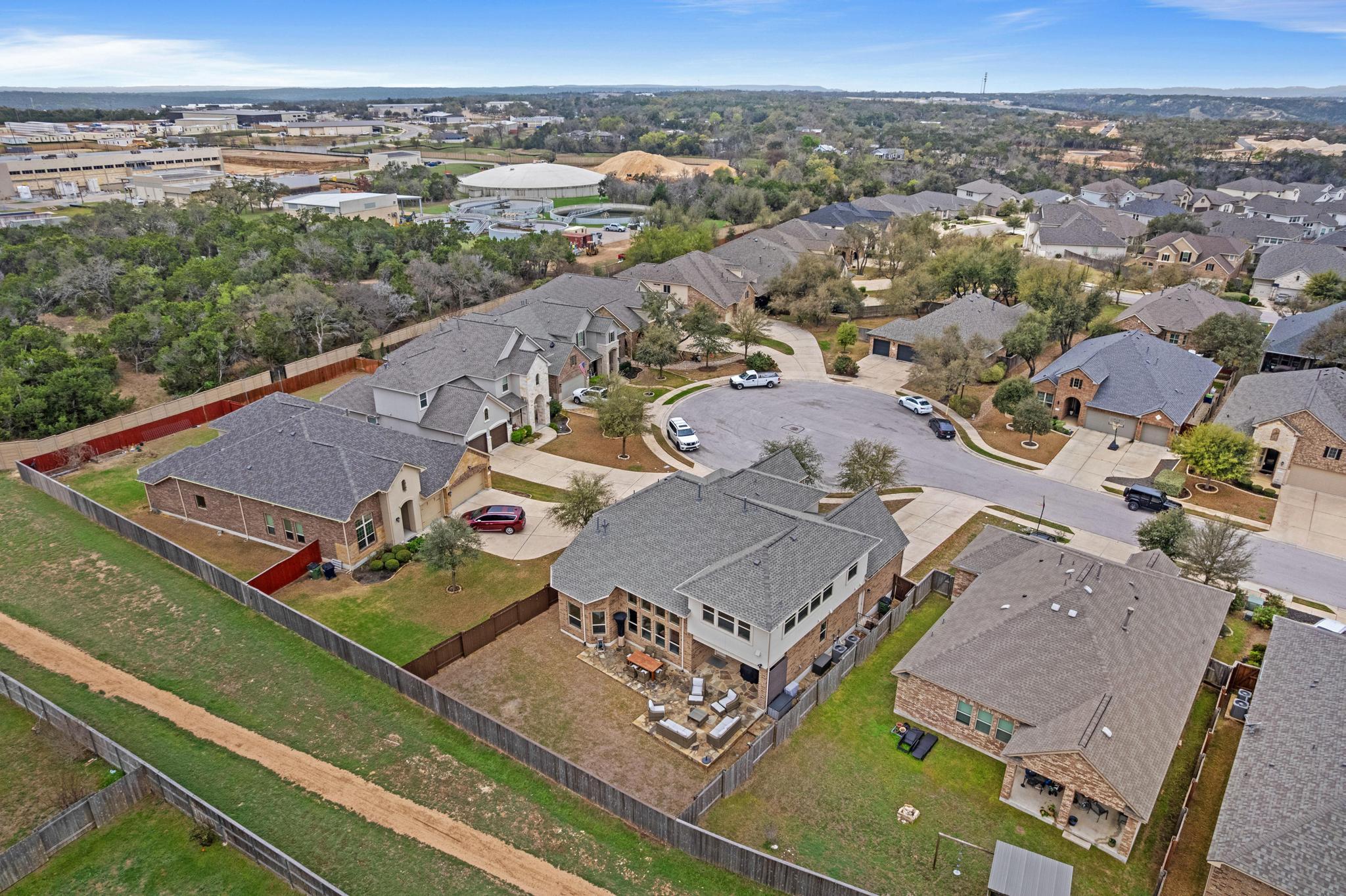 Aerial view of homes around a cul-de-sac, with fenced backyards and wooded land nearby.