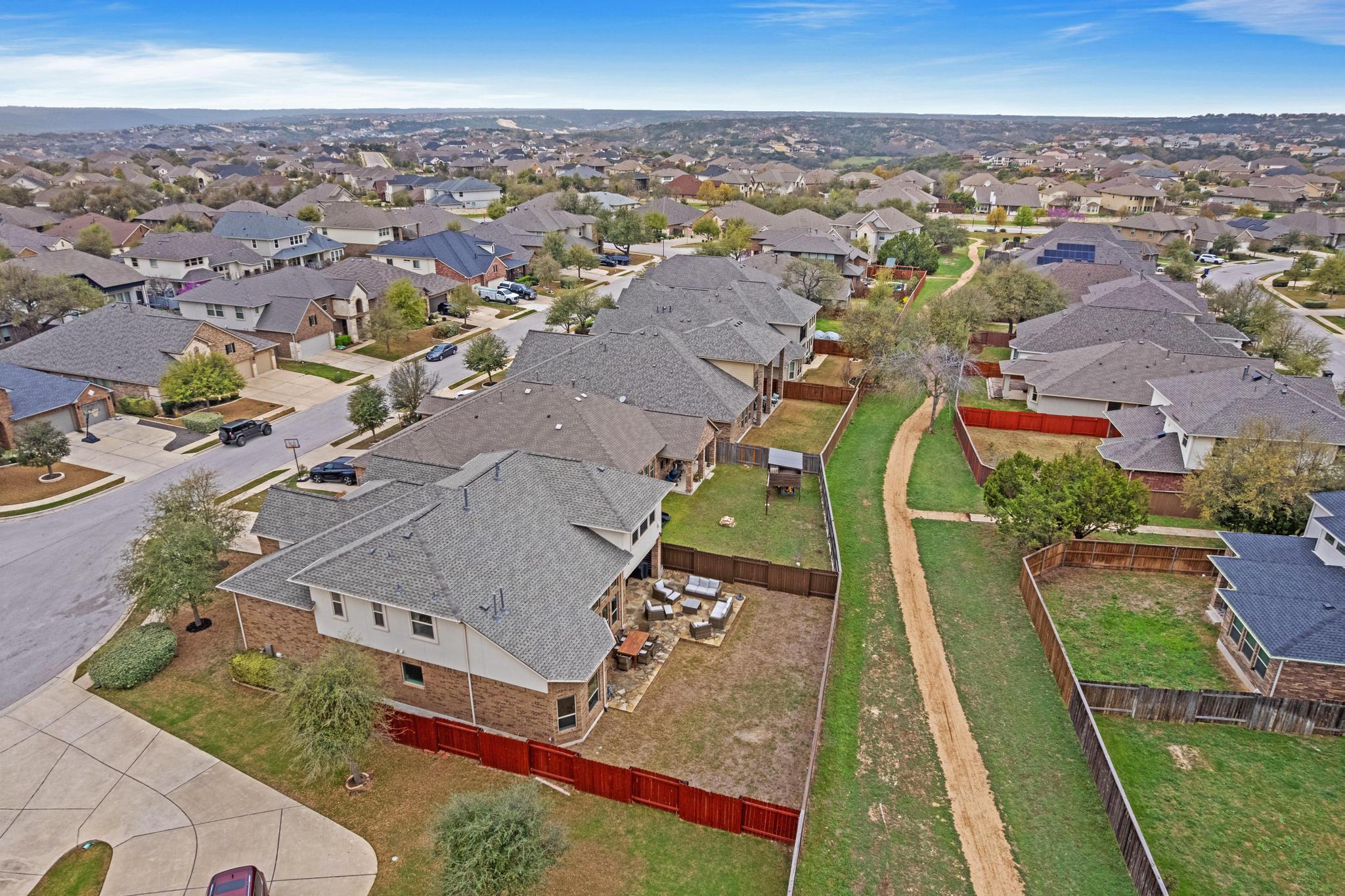Aerial view of a home with a fenced backyard and patio beside a grassy walking path.