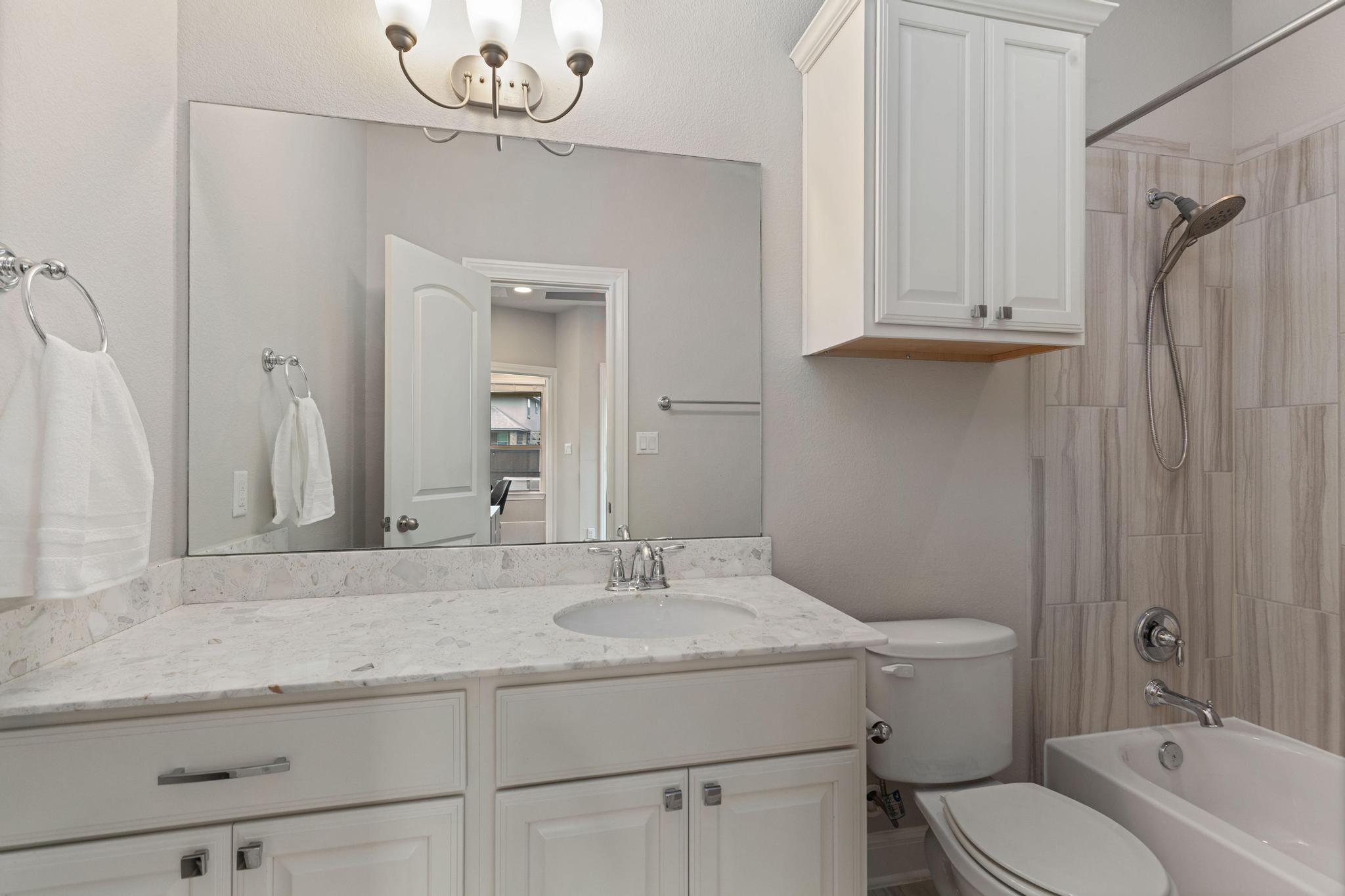 Bathroom with a white vanity, marble-look counter, and tiled tub and shower.