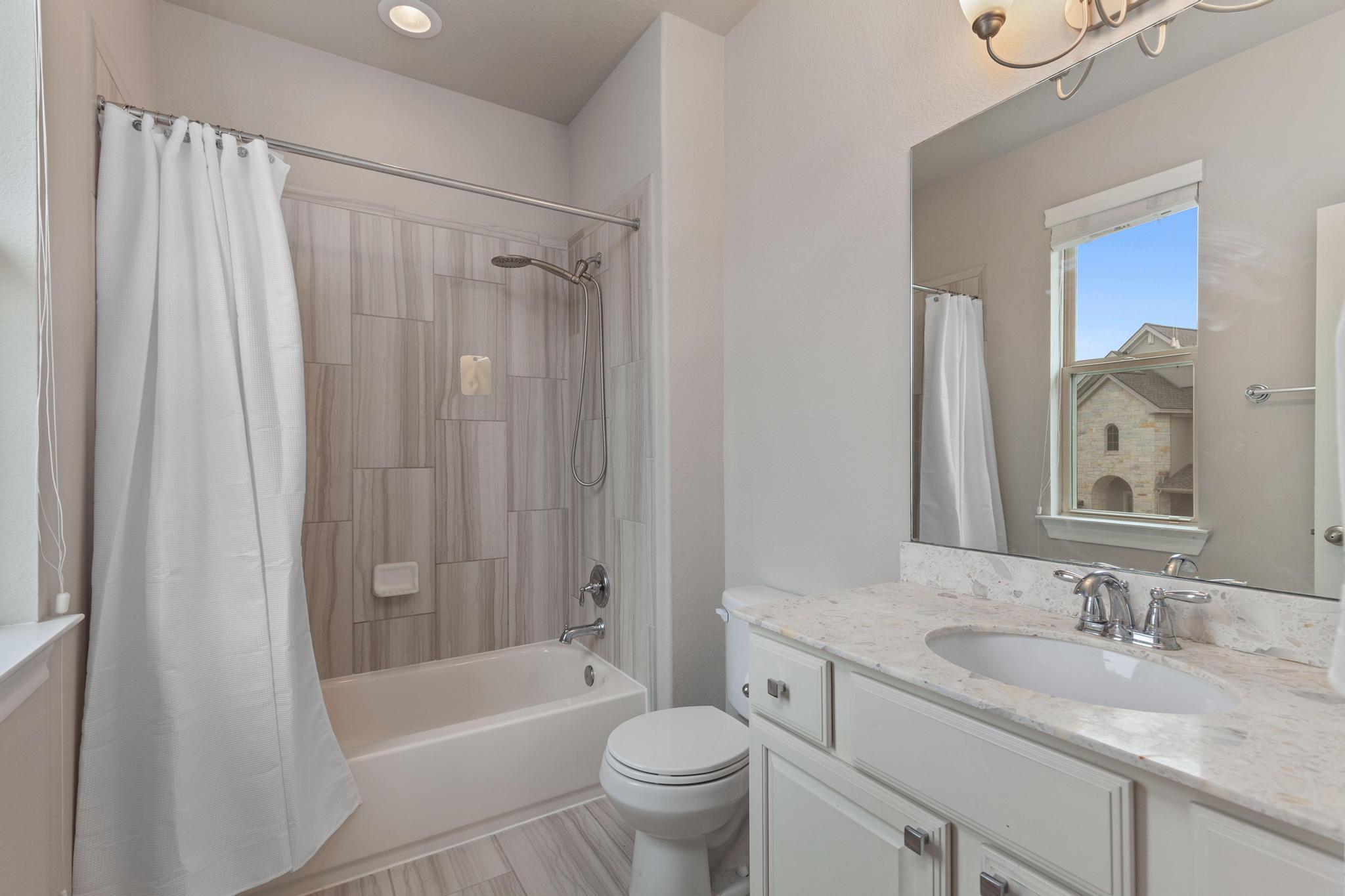 Bathroom with a tiled tub-shower, white vanity, and window overlooking a neighboring home.