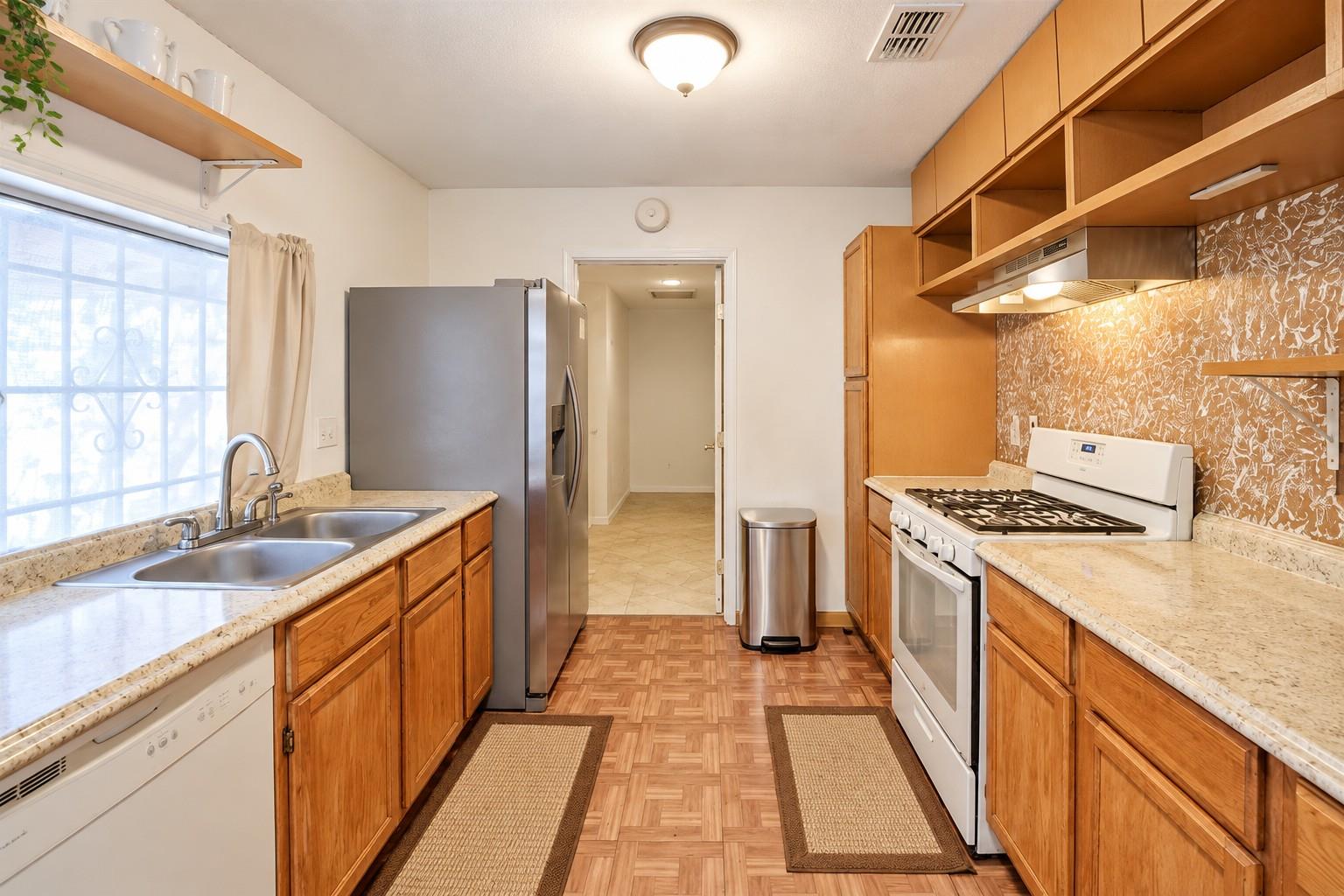 Kitchen with warm wood cabinets, double sink by a window, stainless refrigerator, and white gas range.