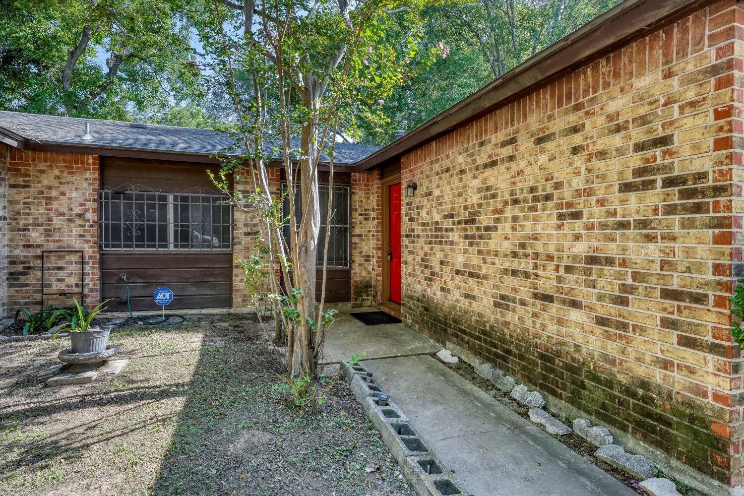 Brick home entry with a bright red door and a shaded concrete walkway.
