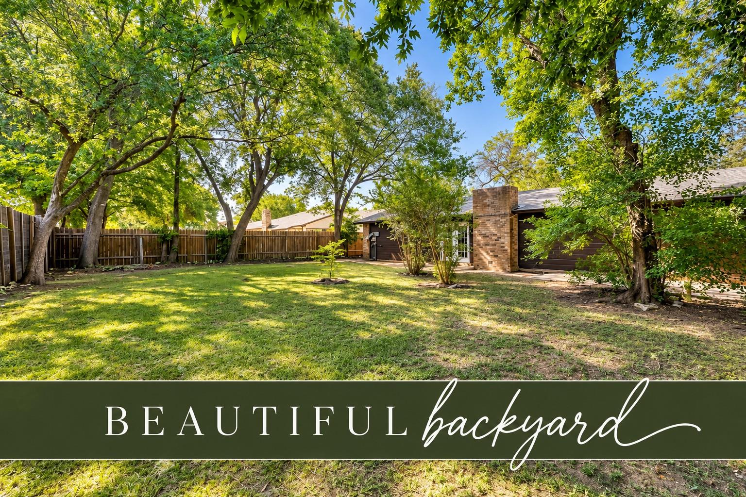 Backyard with a broad lawn, mature shade trees, wood privacy fencing, and the home's brick chimney.