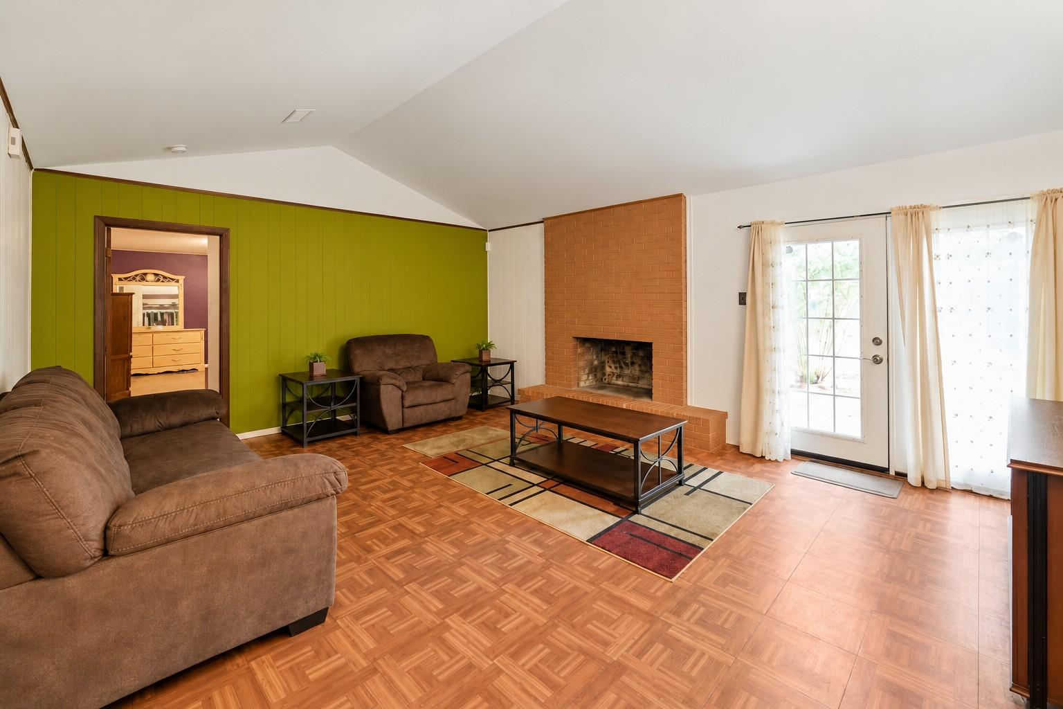 Living room with a brick fireplace, green accent wall, and parquet flooring.