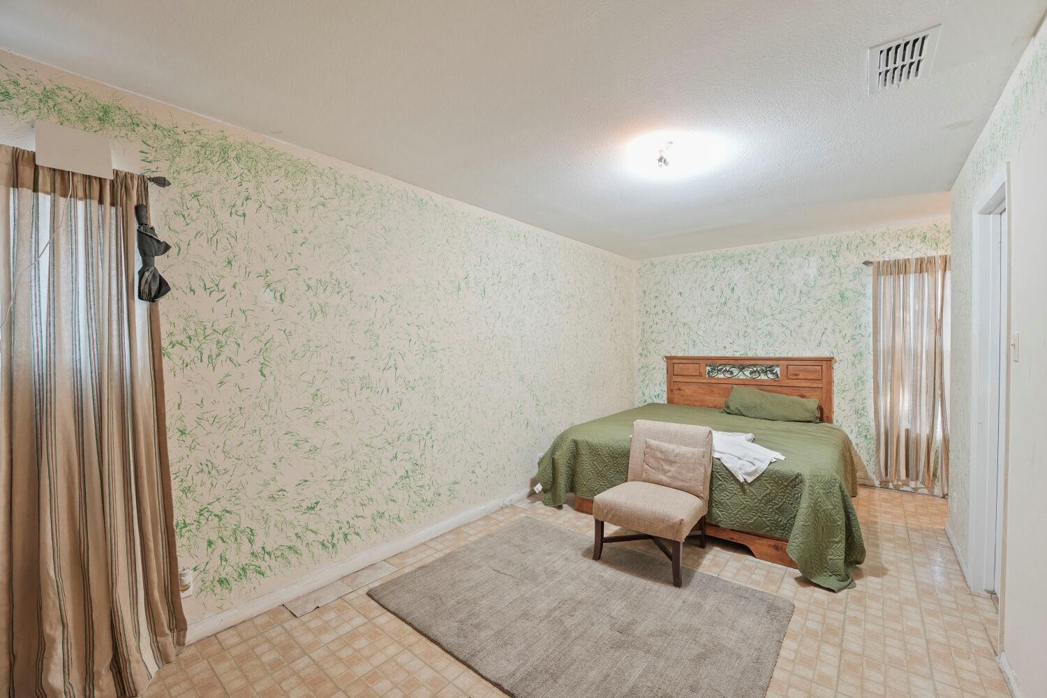 Bedroom with a wooden bed, green quilt, patterned wallpaper, and tiled floor