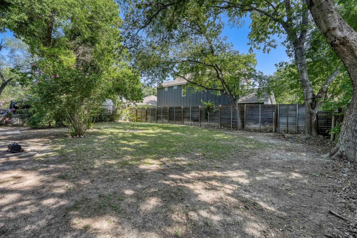 Shaded backyard with mature trees, a wooden privacy fence, and a paved patio.