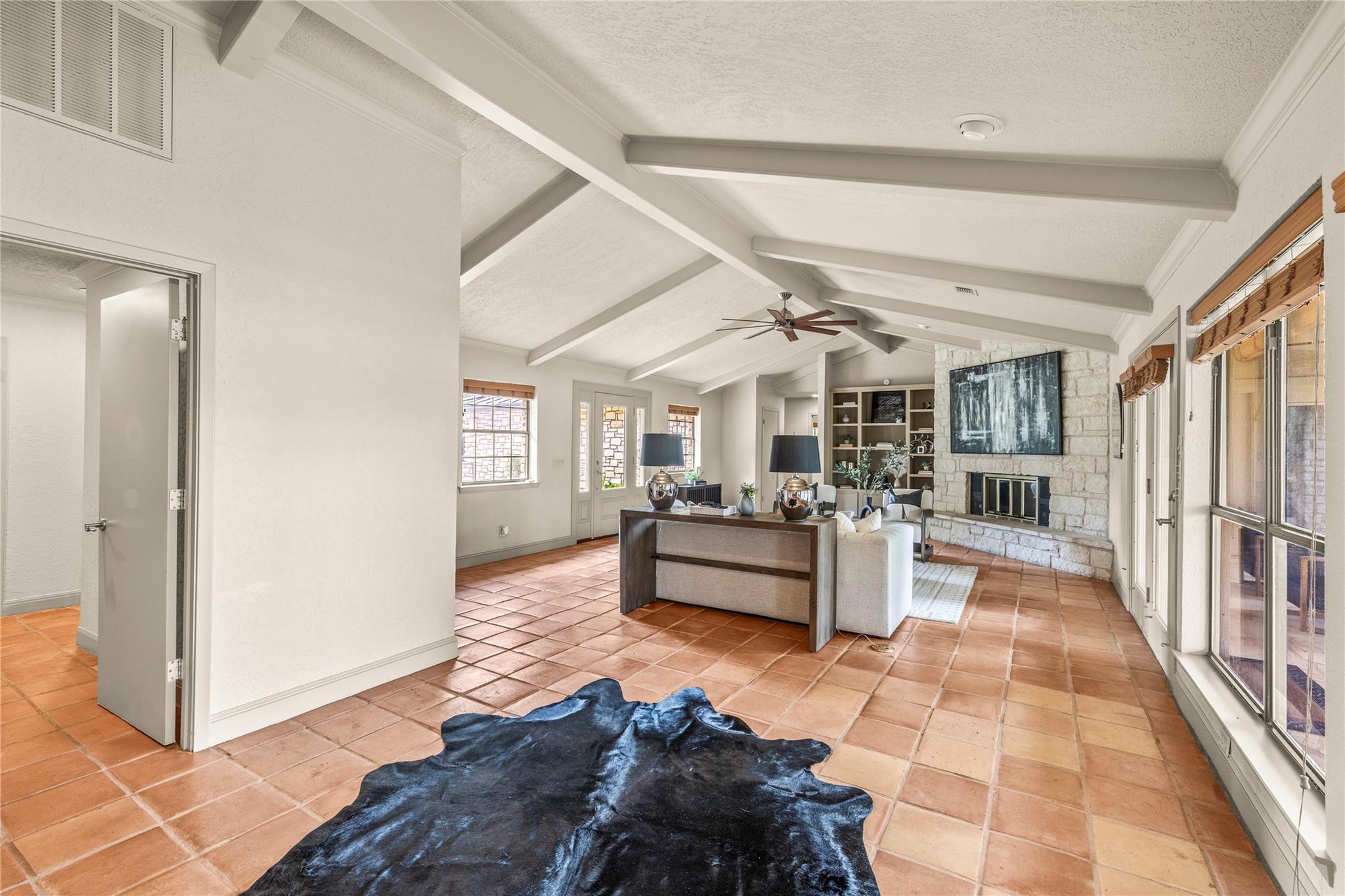 Living room with a vaulted beam ceiling, terracotta tile floors, and a stone fireplace.