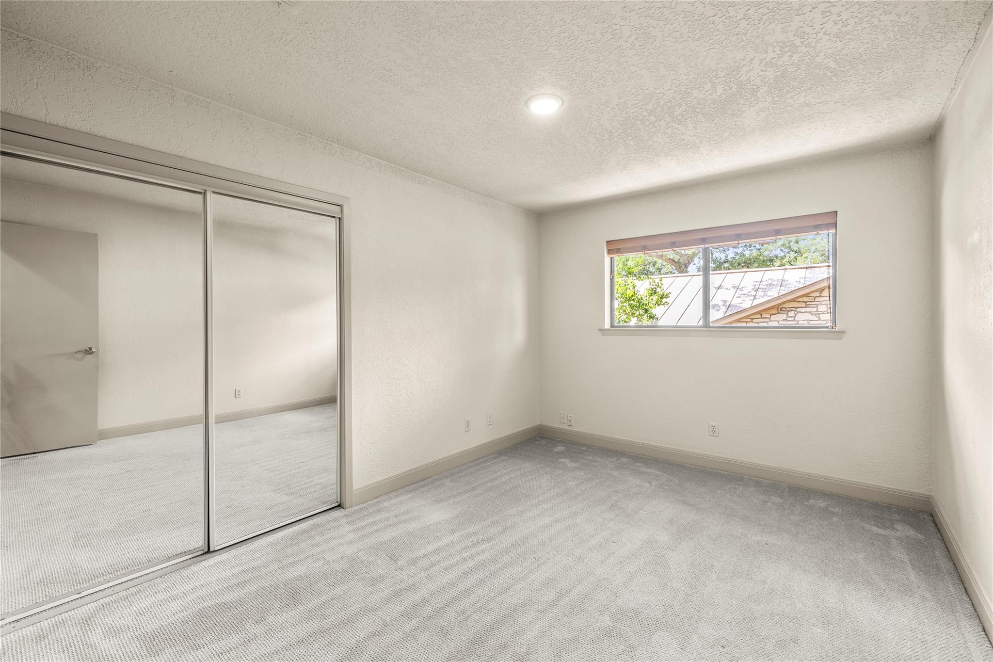 Empty carpeted bedroom with mirrored closet doors and a small window.