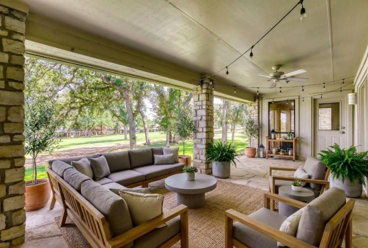 Covered patio with wood-framed lounge seating overlooking a green lawn and mature trees.
