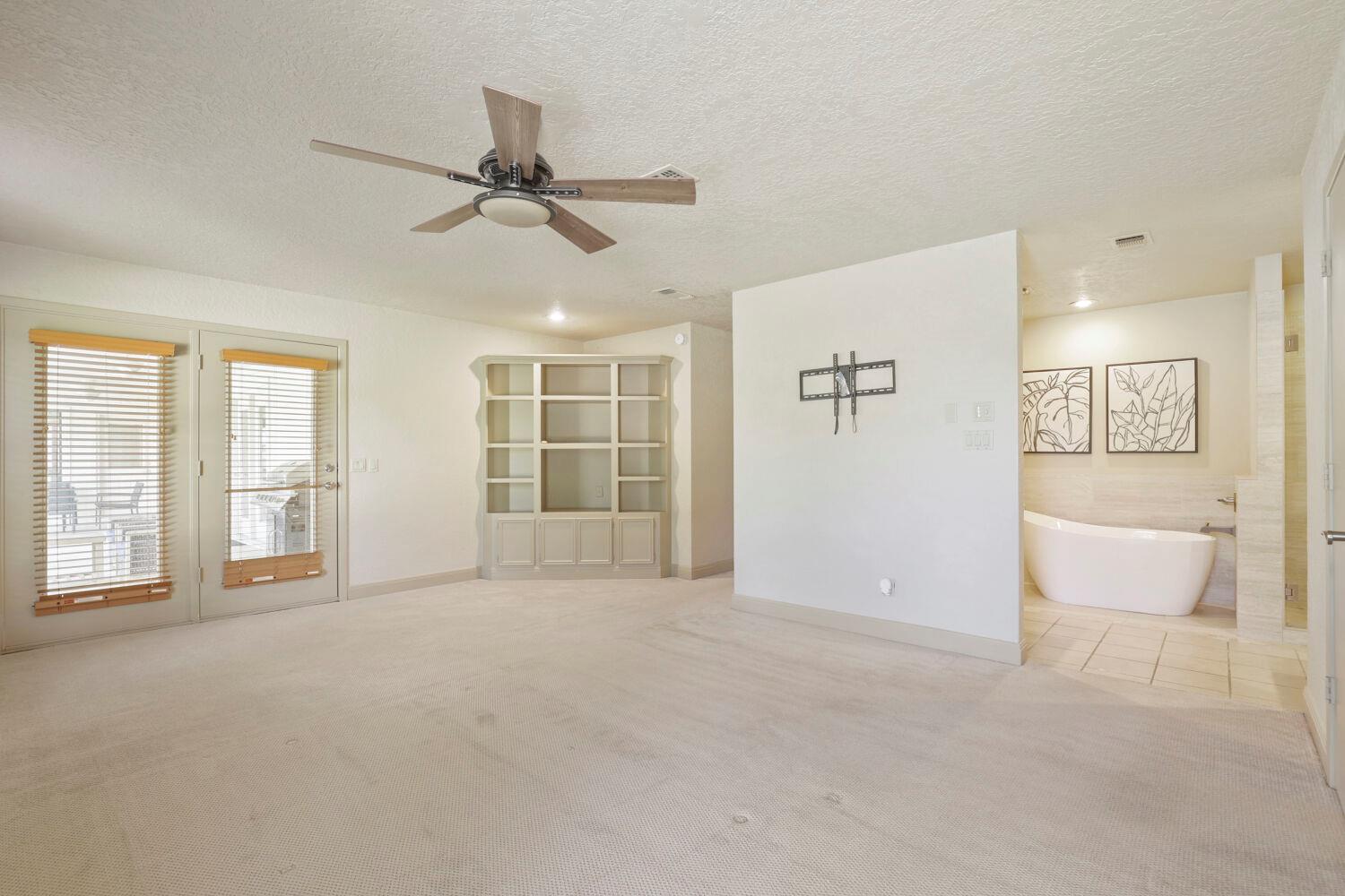 Carpeted bedroom with built-in shelving, glass doors, and an adjoining bathroom with a freestanding tub.