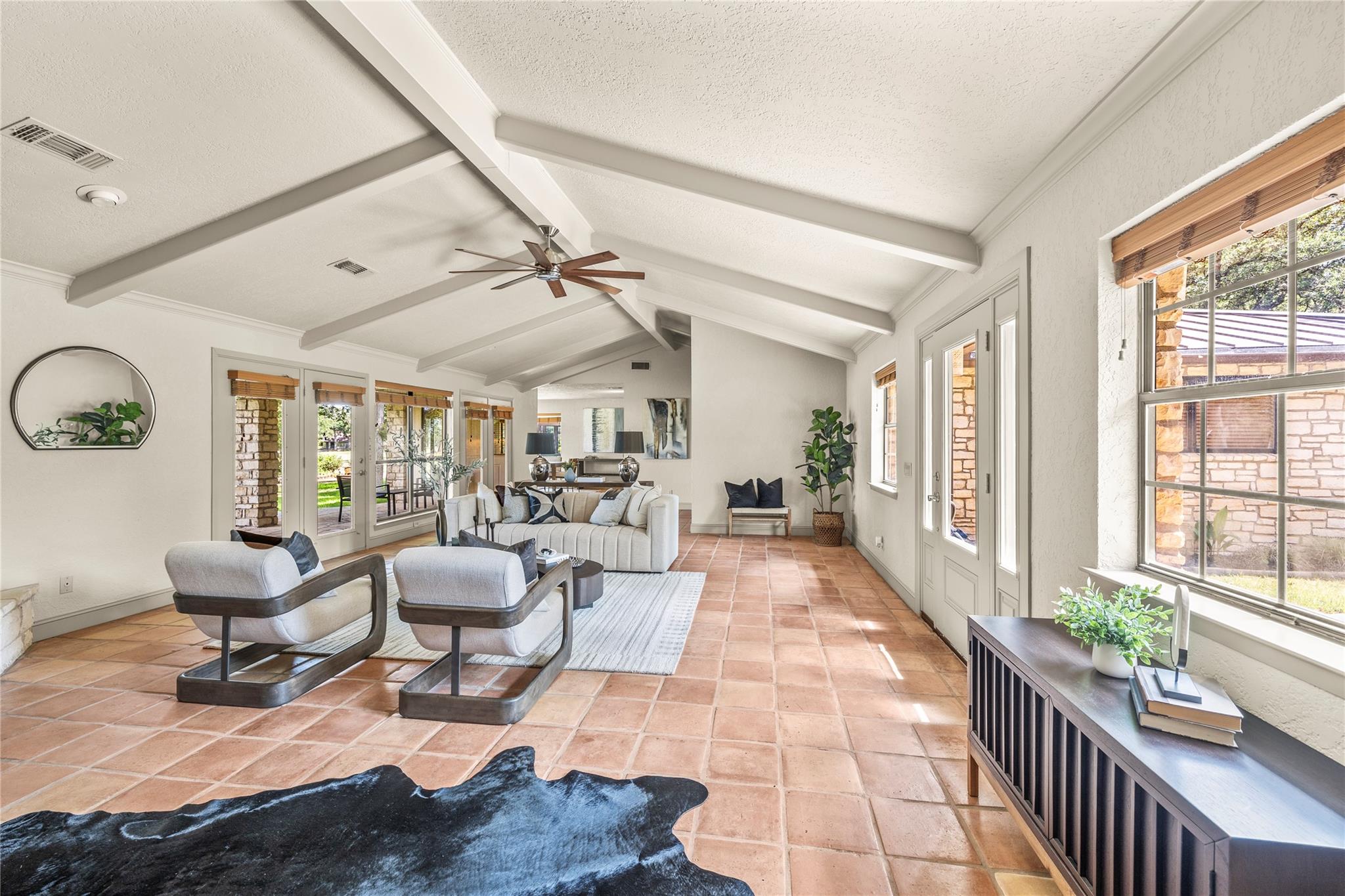 Staged living room with vaulted beamed ceiling, terracotta tile floors, and large windows.