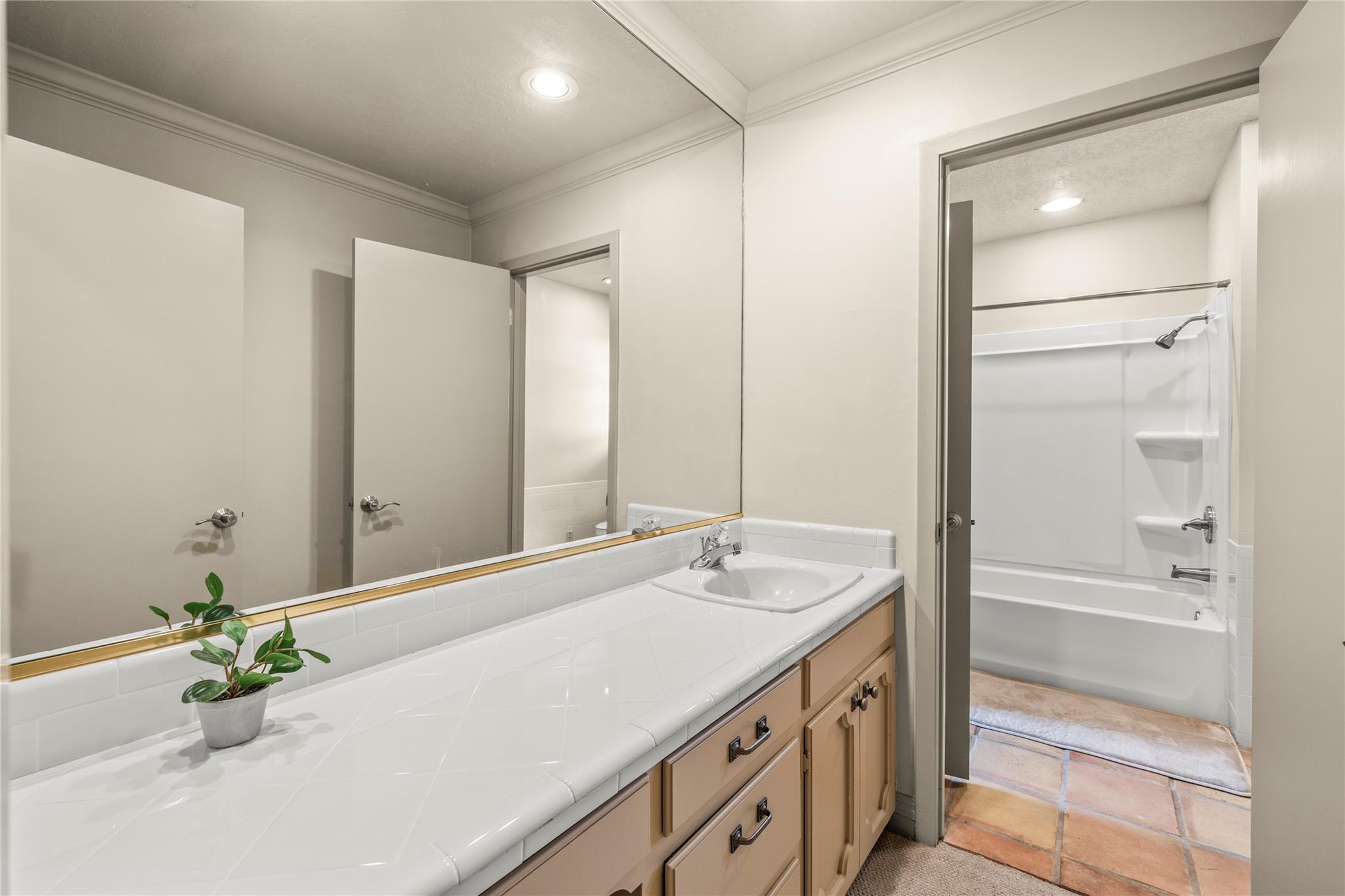 Bathroom with a long tiled vanity and mirror overlooking a tub and shower.