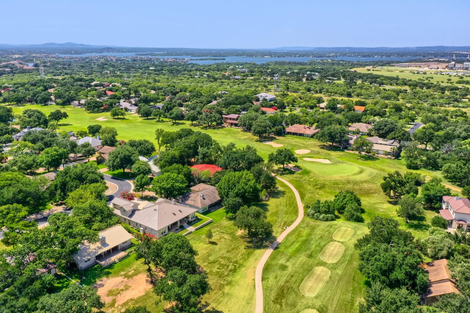 Aerial view of homes beside a golf course, with a lake visible in the distance.