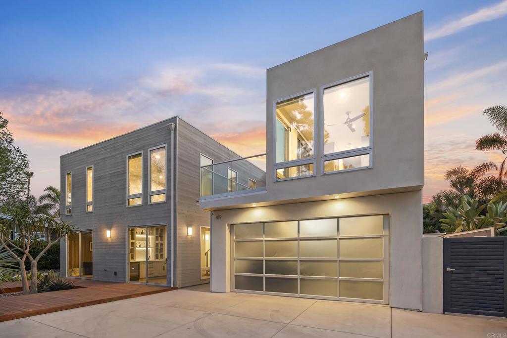 Modern two-story home with a glass balcony and wide garage door at dusk.
