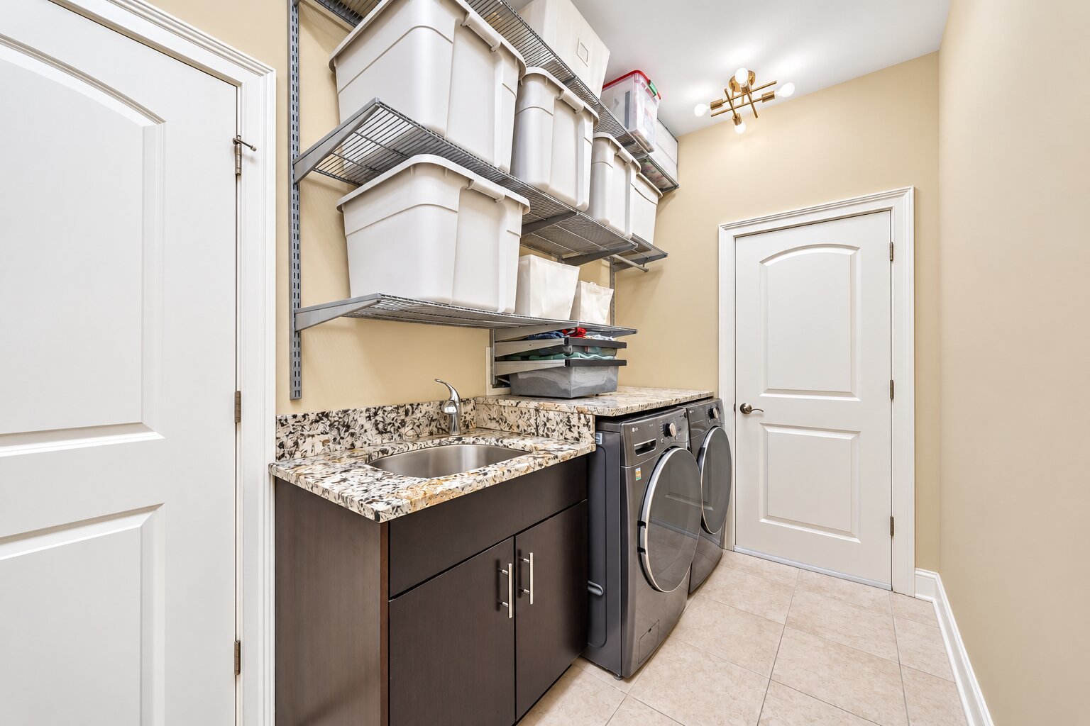 Laundry room with front-loading washer and dryer, granite counter, sink, and wall-mounted storage shelves.