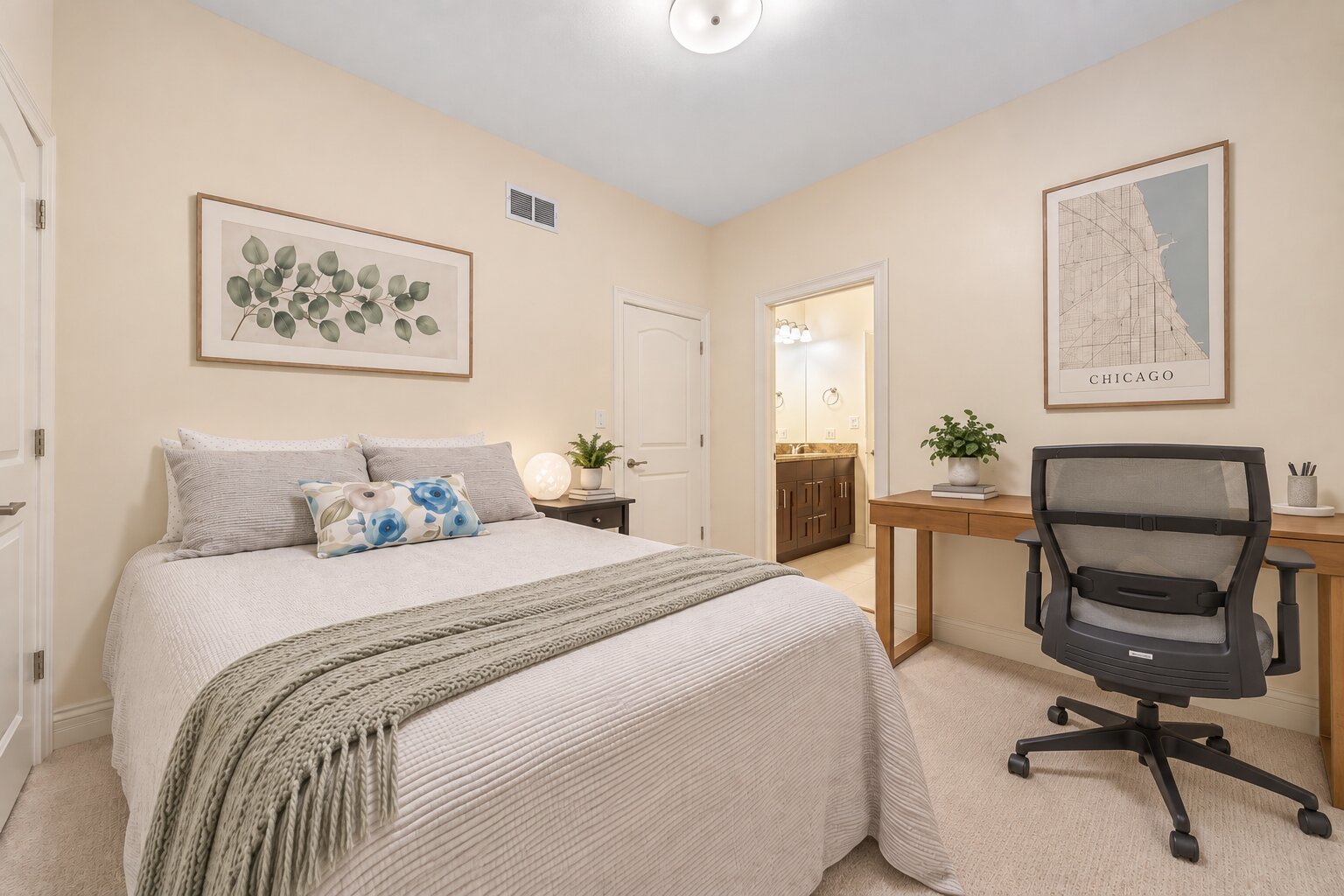 Furnished bedroom with a large bed, desk, office chair, and open ensuite bathroom doorway.