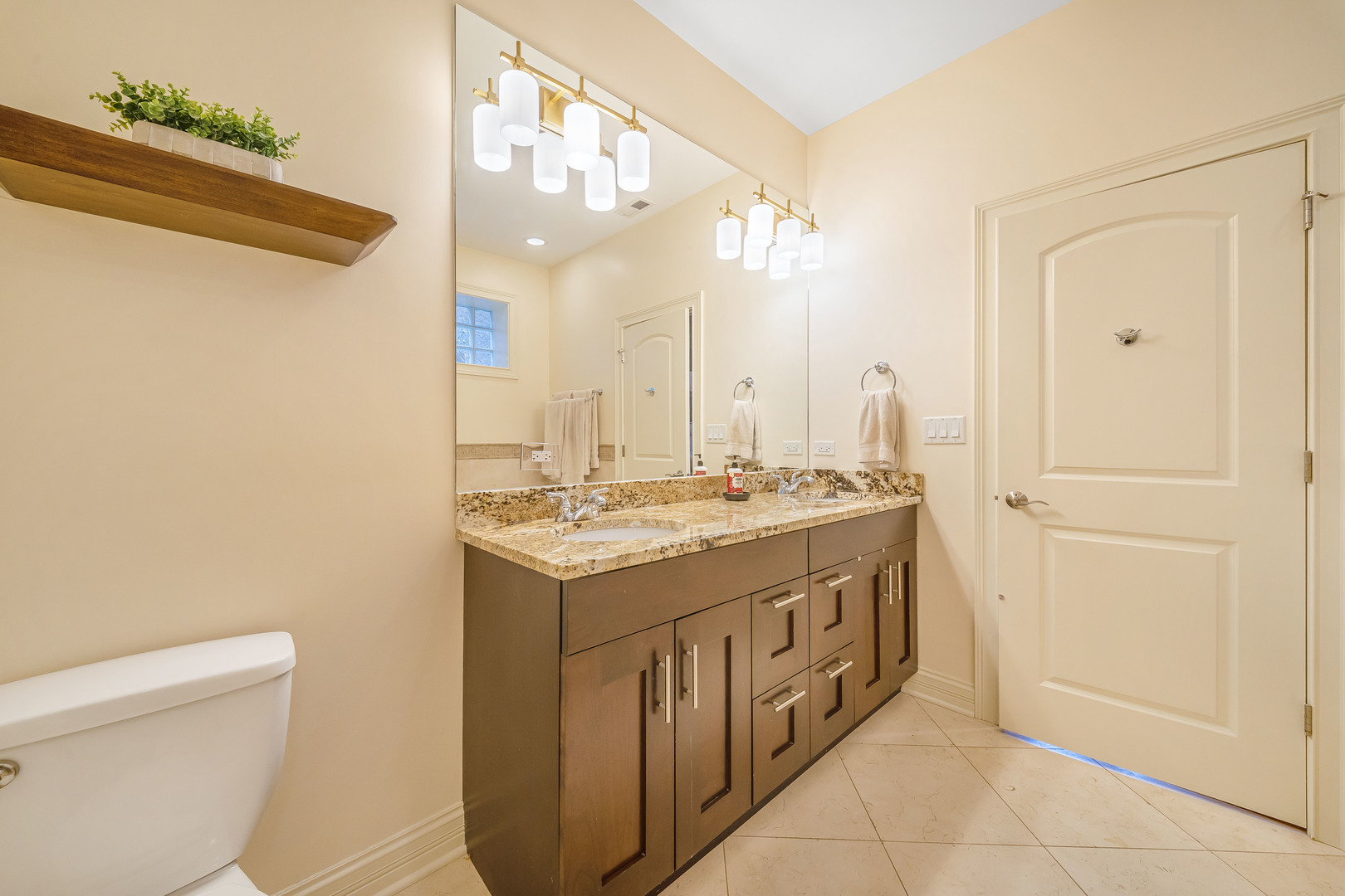 Bathroom with a granite double-sink vanity, dark wood cabinets, and a large mirror.